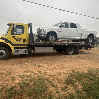 A yellow tow truck is towing a white truck.