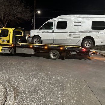 A tow truck is towing a rv down a street at night.