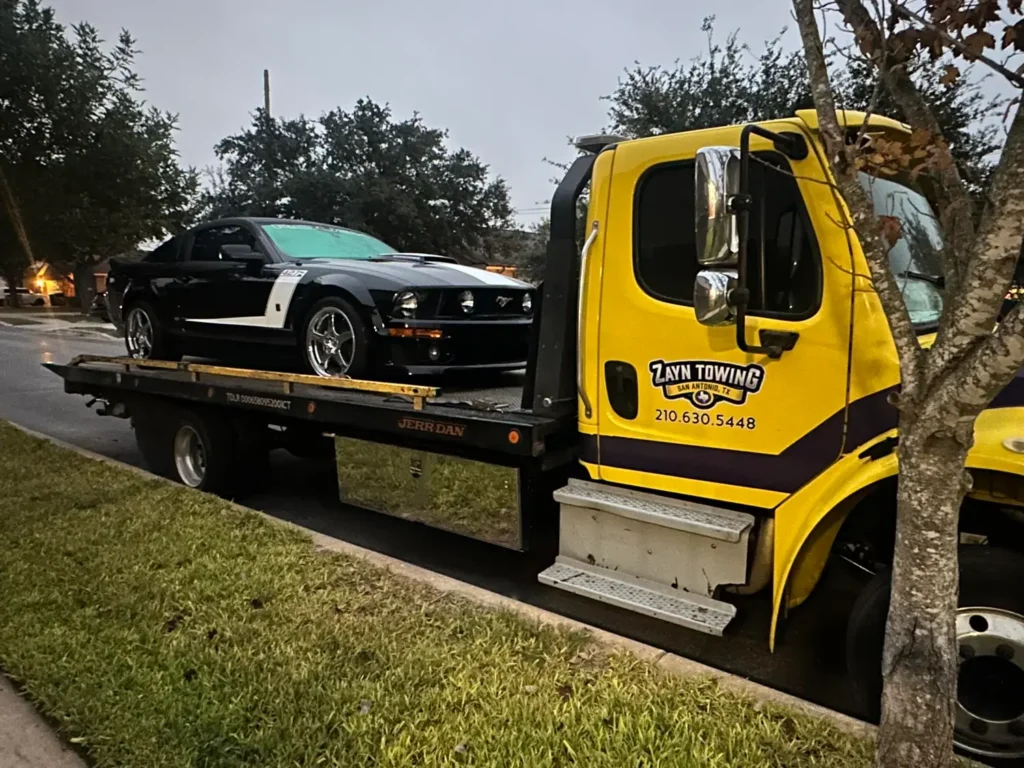 A yellow tow truck is carrying a black mustang on the back of it.