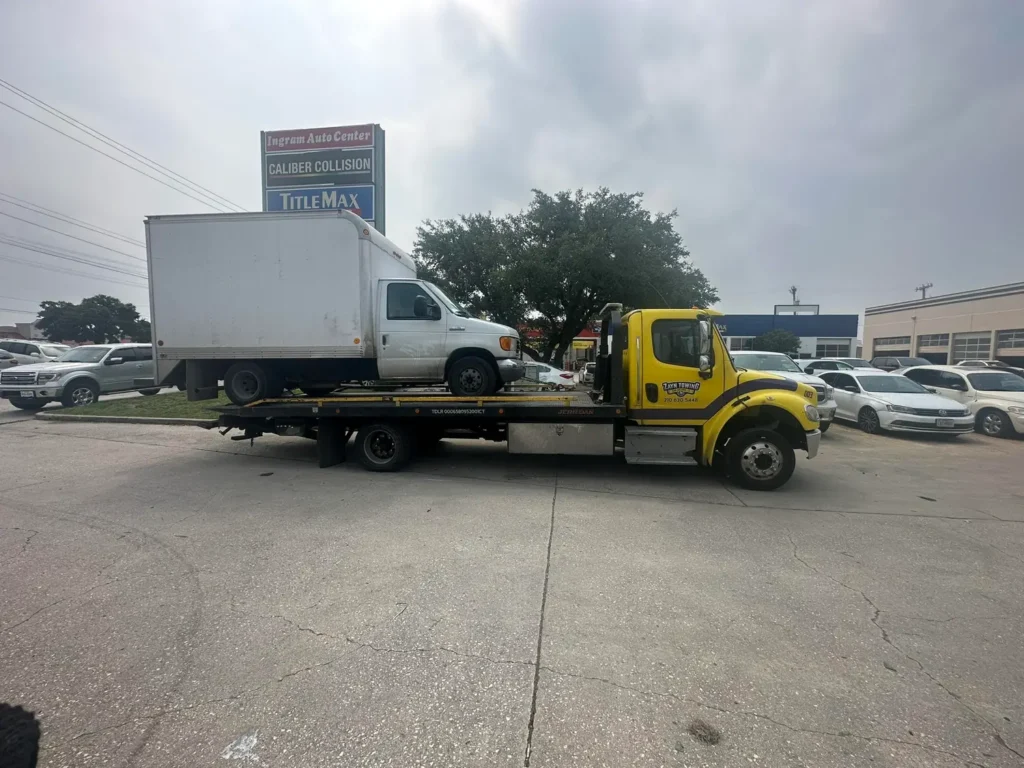 A yellow tow truck is towing a white truck in a parking lot.