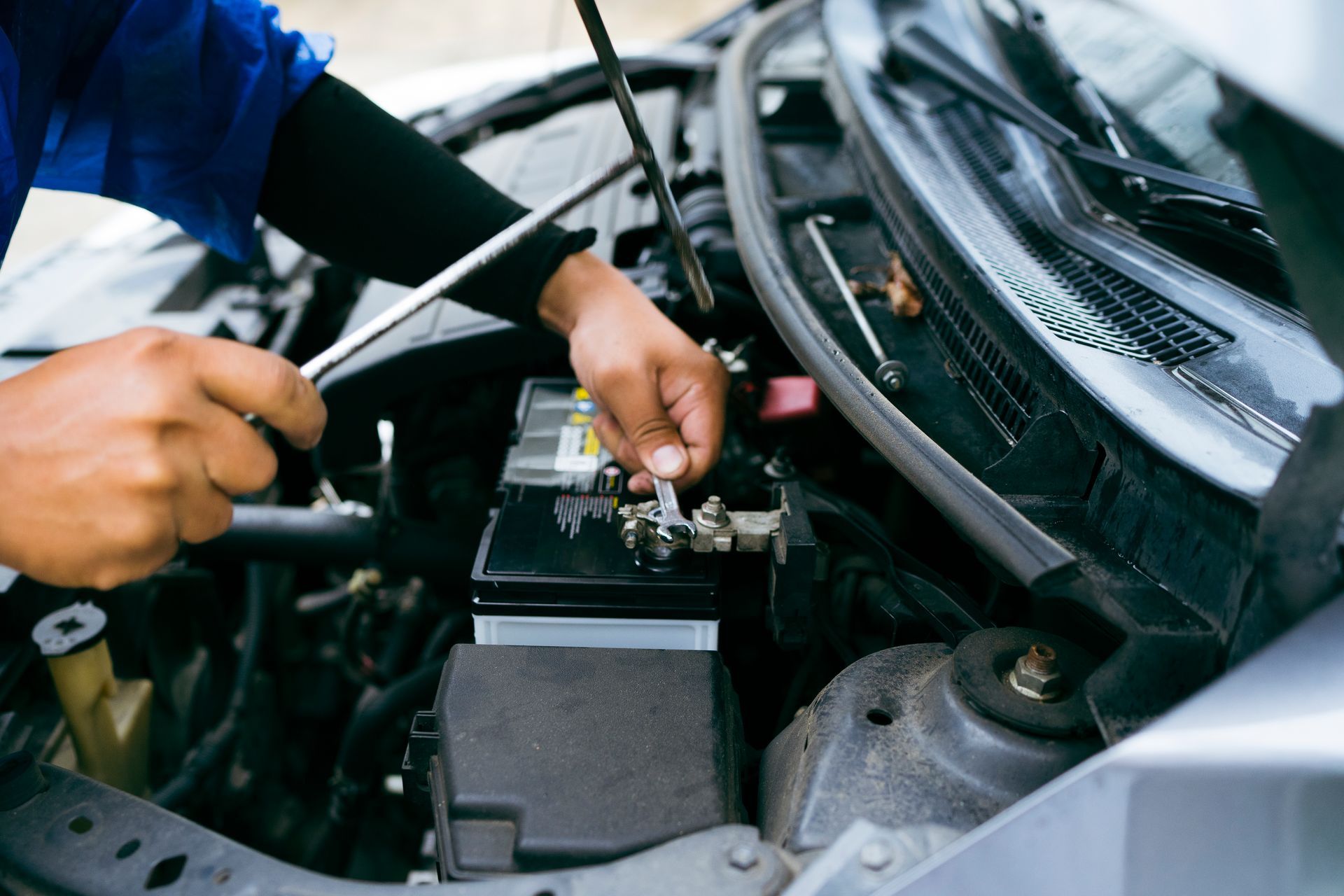 A man is working on a car battery with a wrench.
