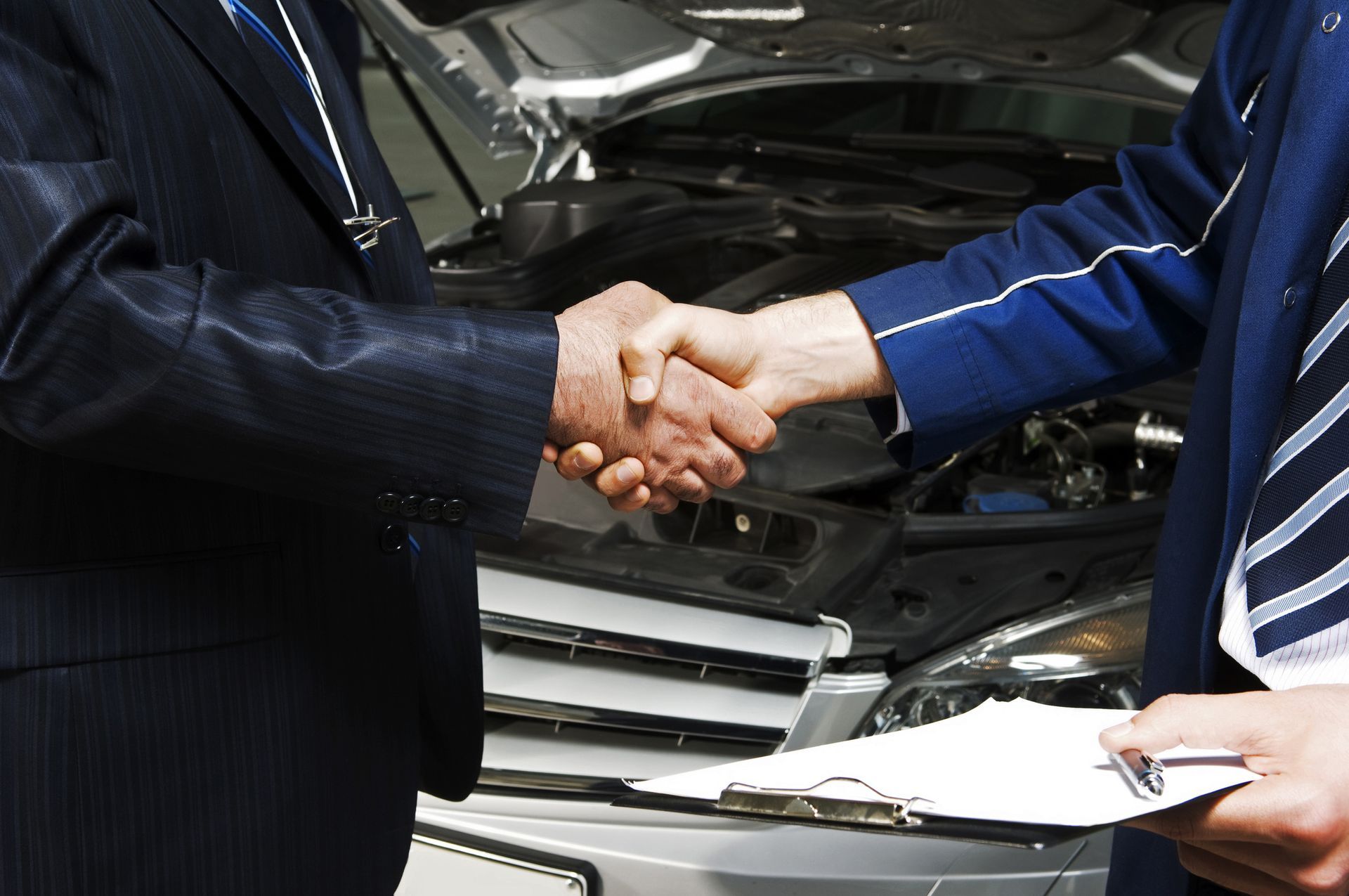 Two men shaking hands in front of a car