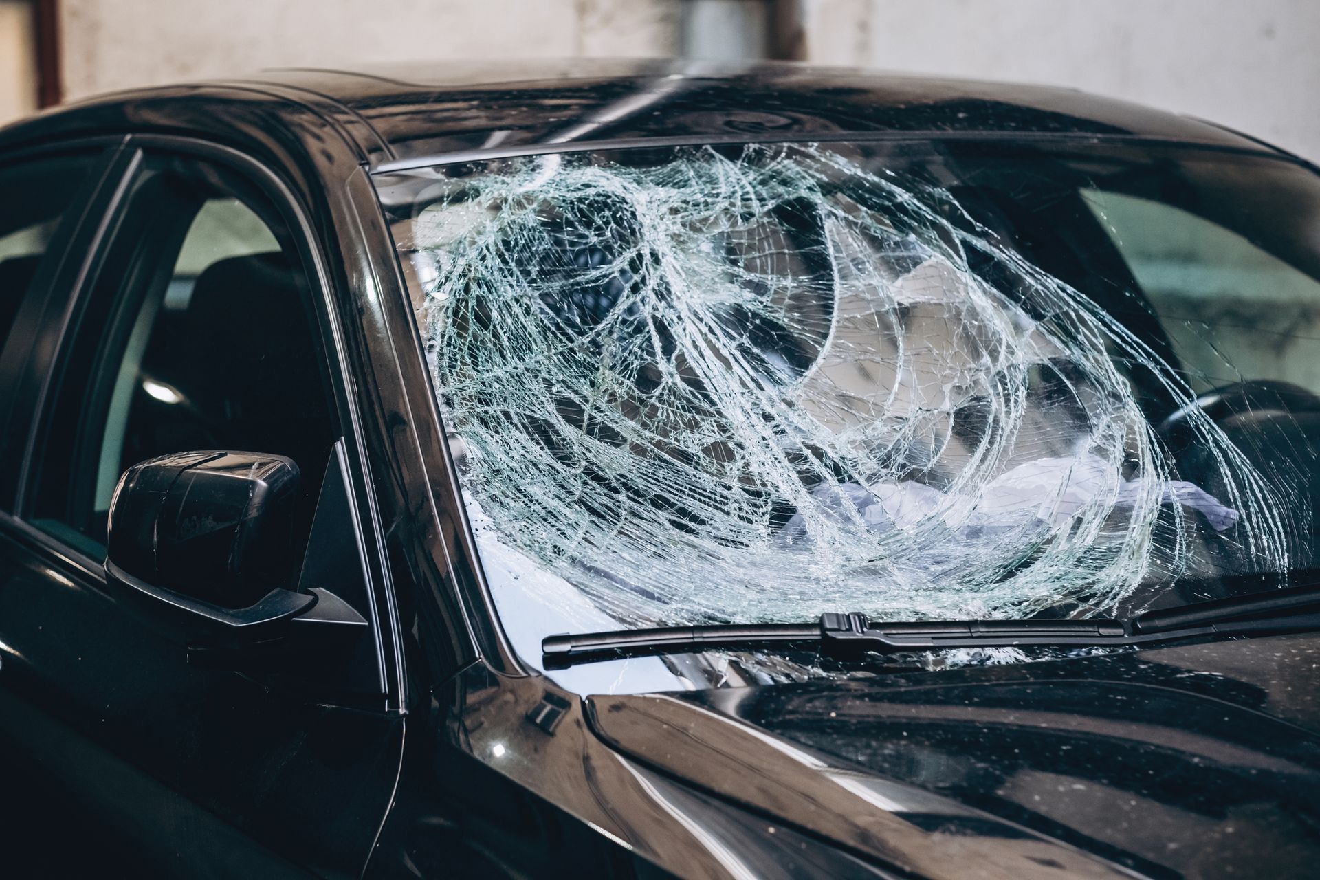 A black car with a broken windshield is parked in front of a building.