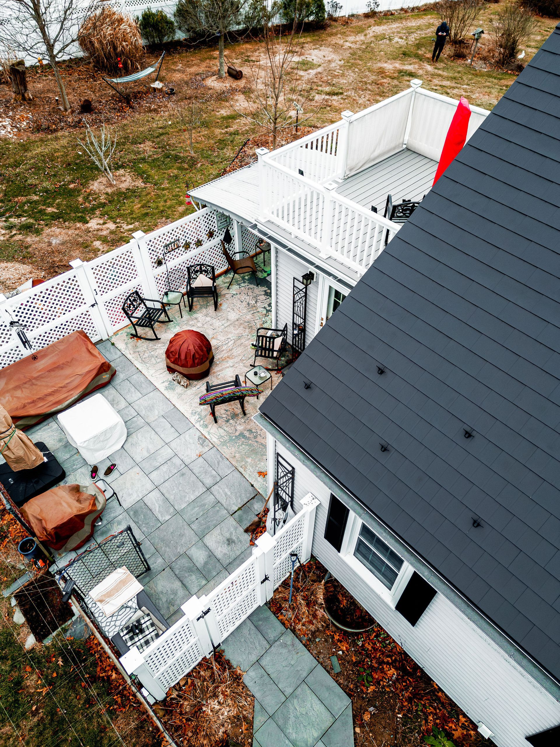 Aerial view of a house with a grey roof and white deck. Outdoor seating area with a red fire pit.