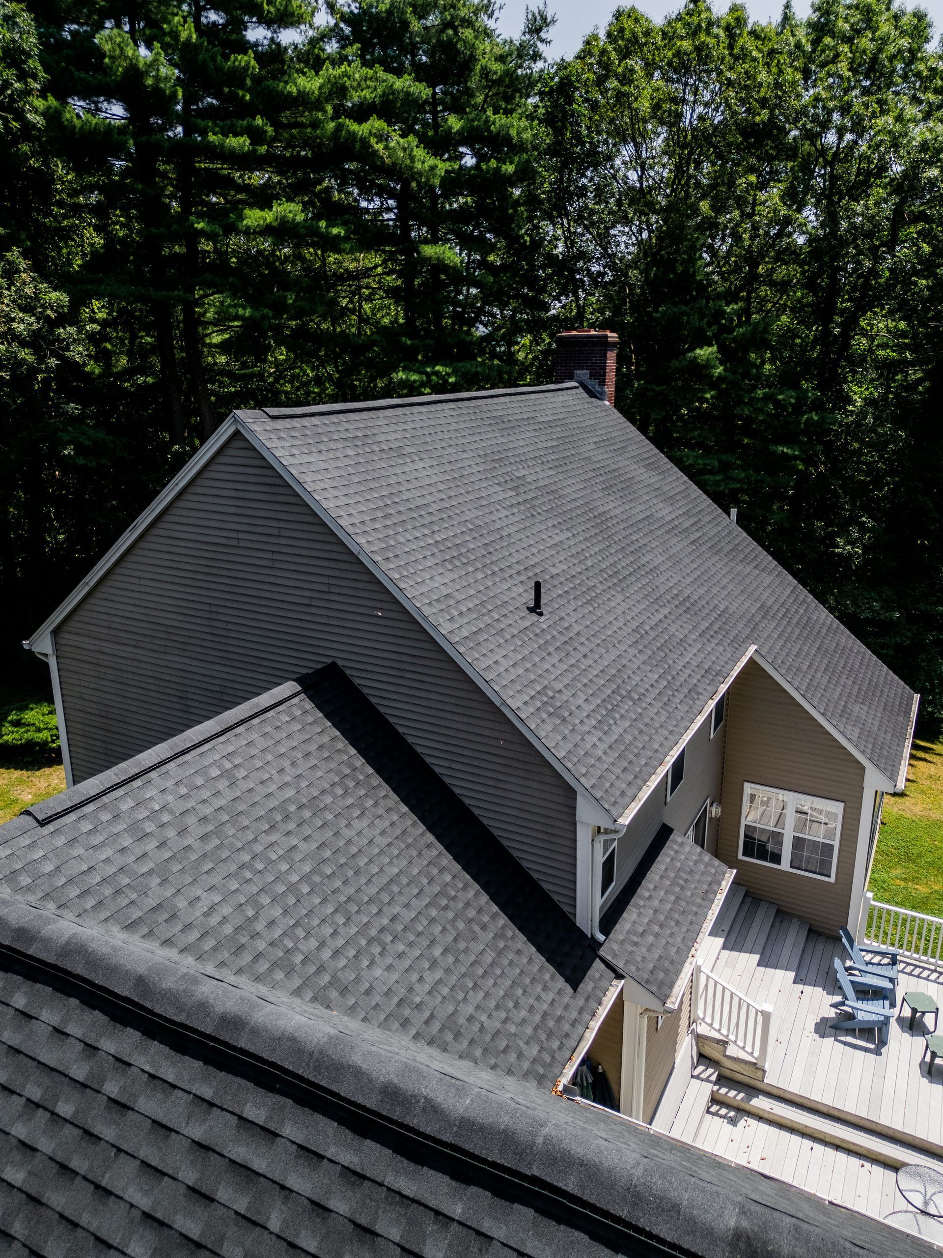 Gray asphalt shingle roof of a house surrounded by trees, with a wooden deck.