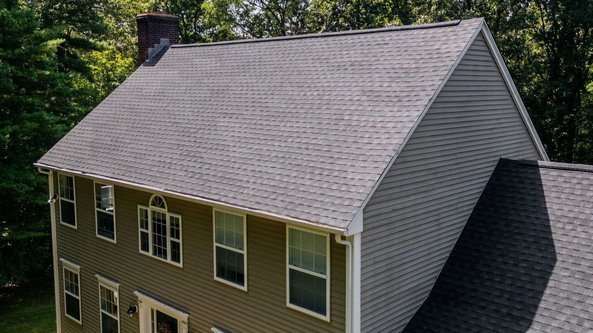 Two-story house with gray roof, green siding, white trim, and a brick chimney surrounded by trees.