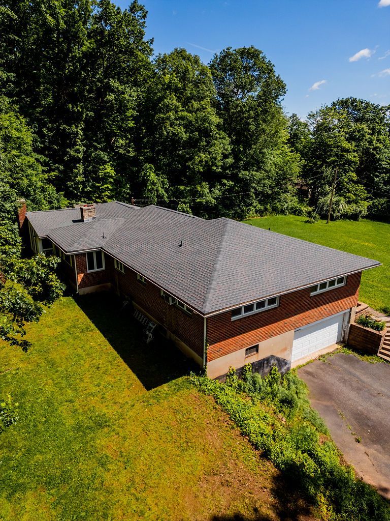 A brick ranch-style house with a gray roof, surrounded by trees and grass, under a blue sky.
