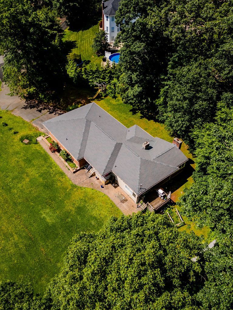 Aerial view of a house with a dark roof surrounded by green trees and lawn.
