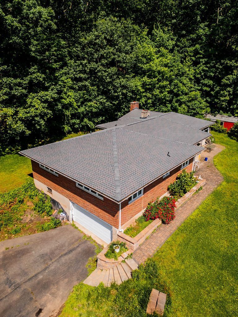 An aerial view of a brick house with a grey roof surrounded by trees and a driveway.