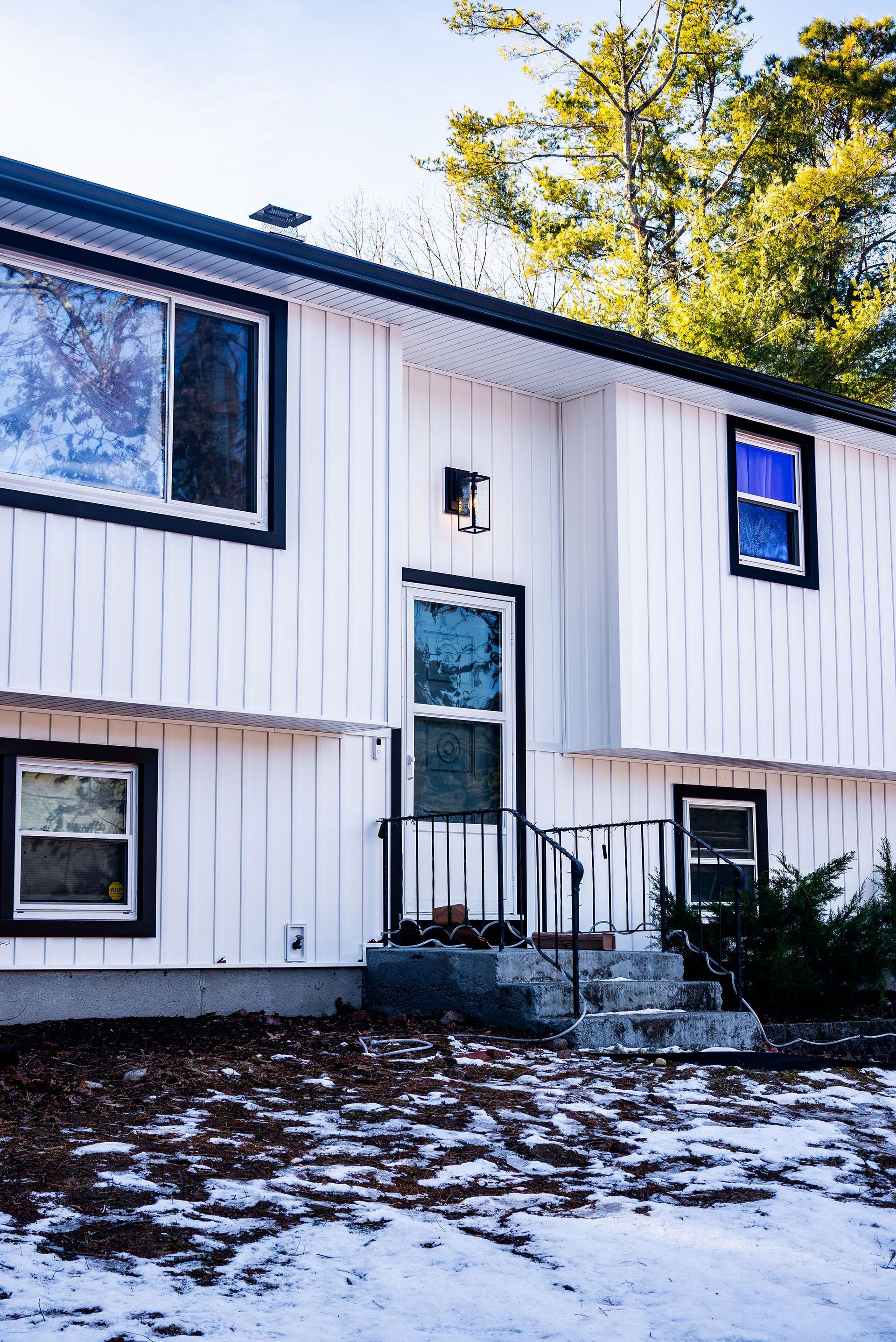 White two-story house with black trim, door with frosted glass, and snow on the ground.