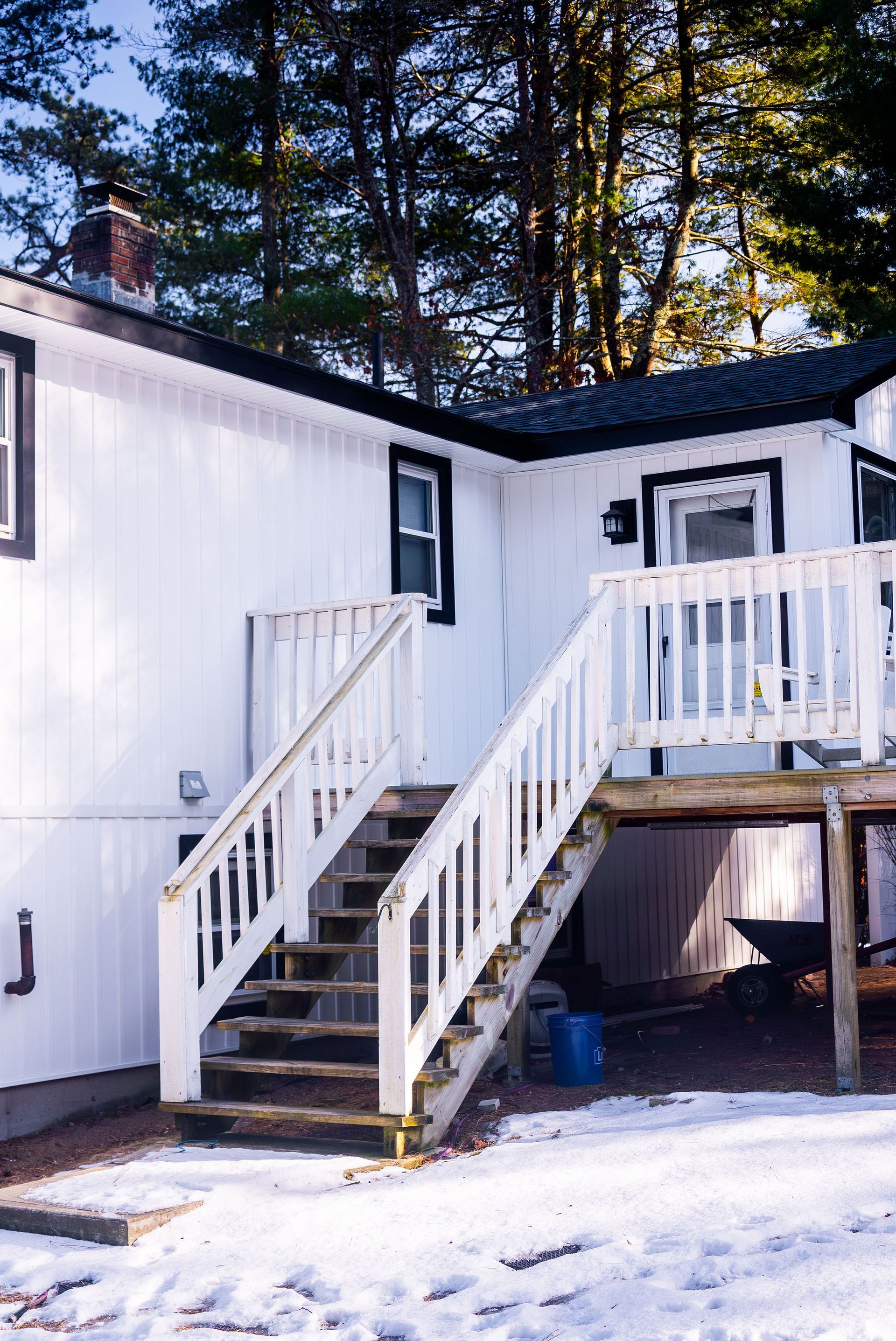 White house with outdoor stairs and deck, snowy ground.