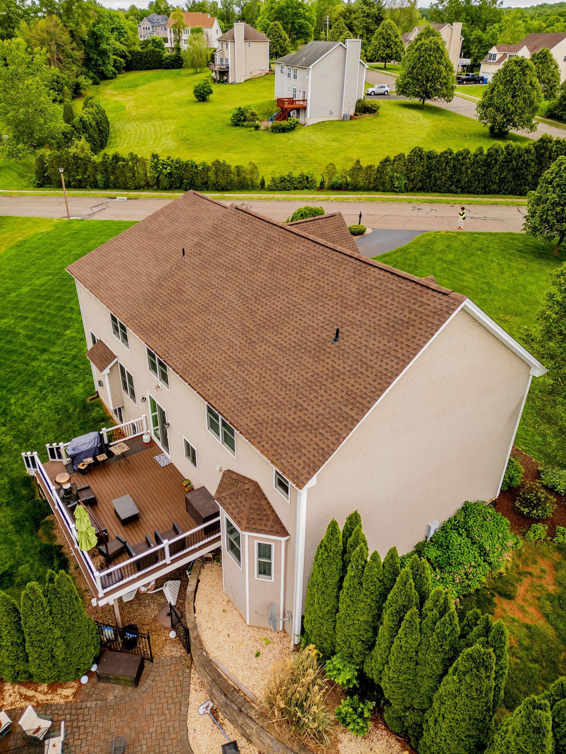 Two-story house with brown roof, wooden deck, and green lawn.