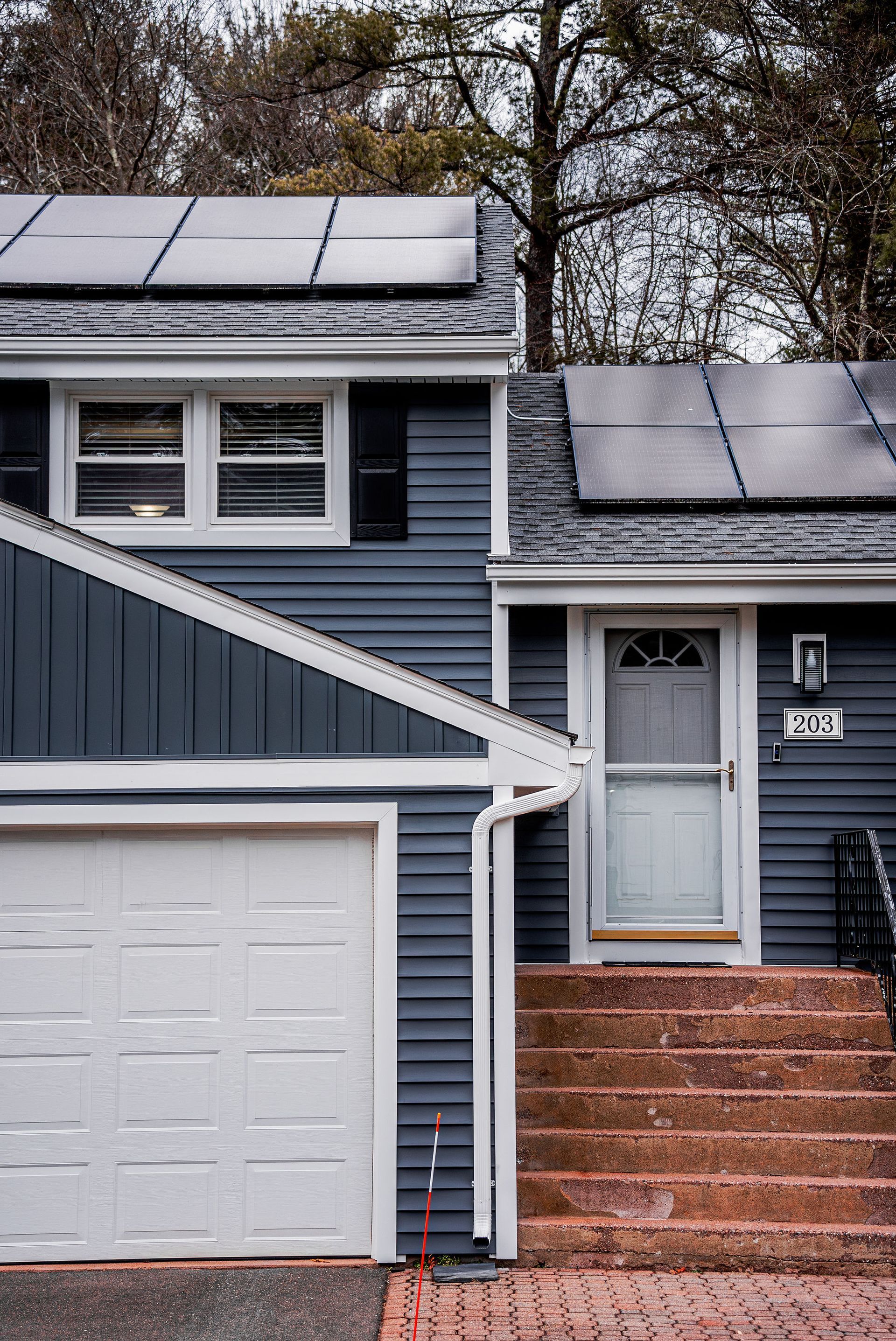House exterior with blue siding, white garage door, and solar panels on the roof. Steps lead to a white door.