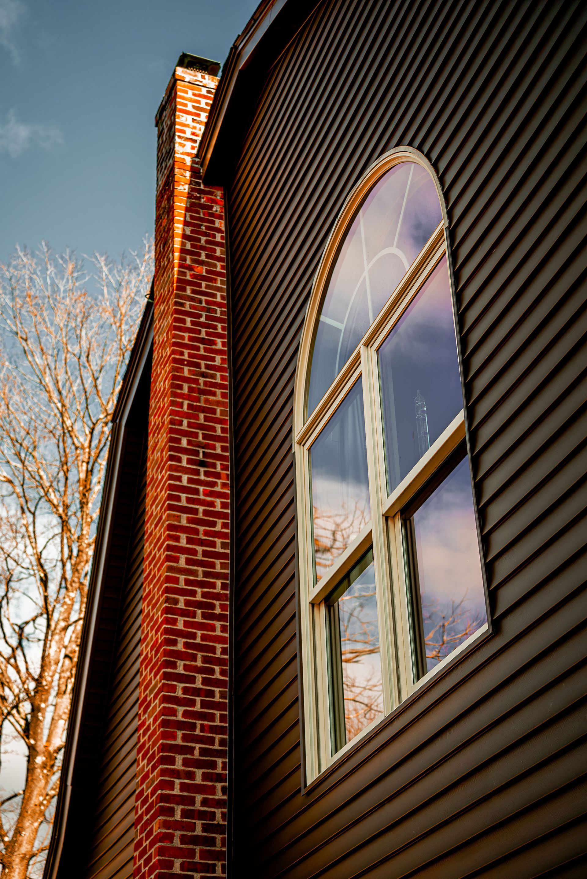 Brown building with arched window, brick chimney, and a tree against a blue sky.