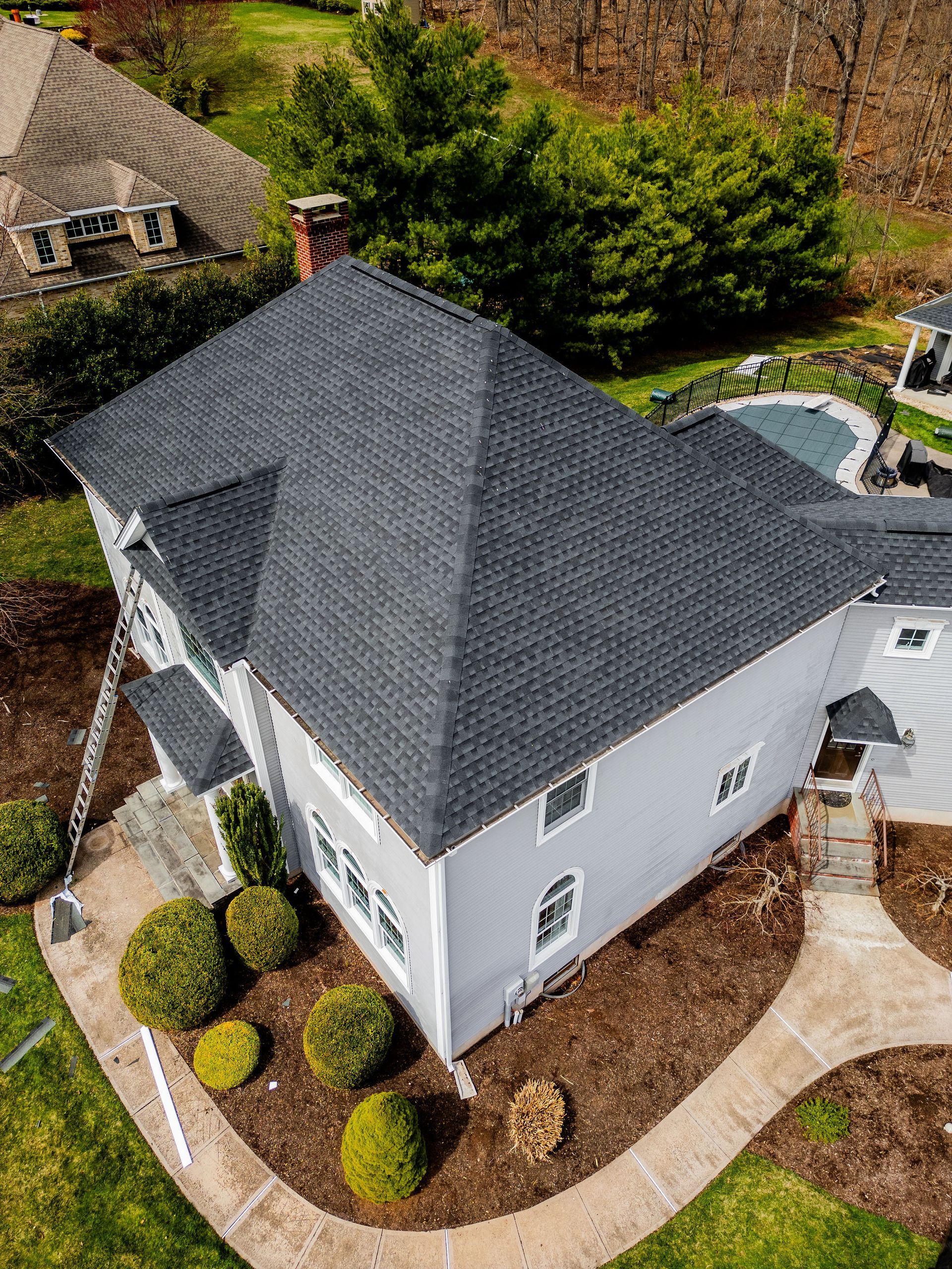 Overhead view of a light gray two-story house with a dark gray roof, surrounded by green landscaping and a walkway.