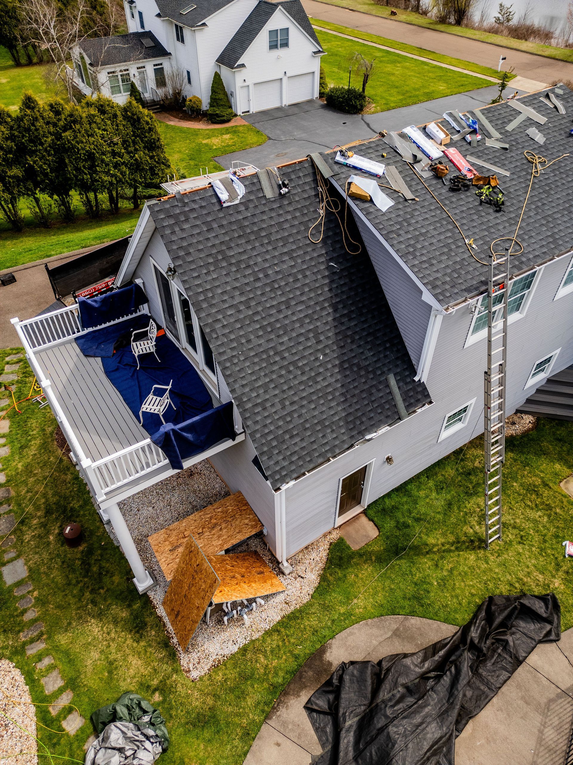 Damage to a house roof after a storm, with debris scattered, blue patio, and a ladder.
