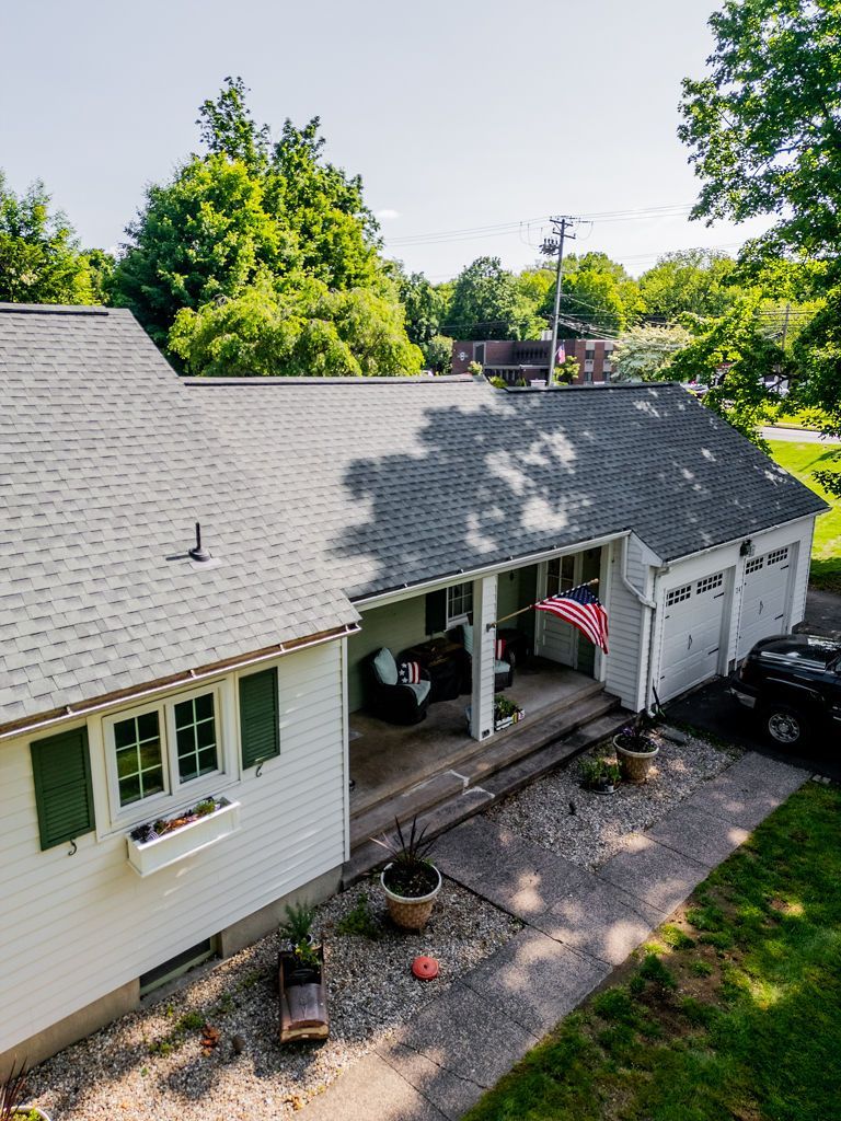 White house with gray roof, covered porch, American flag, and three-car garage.
