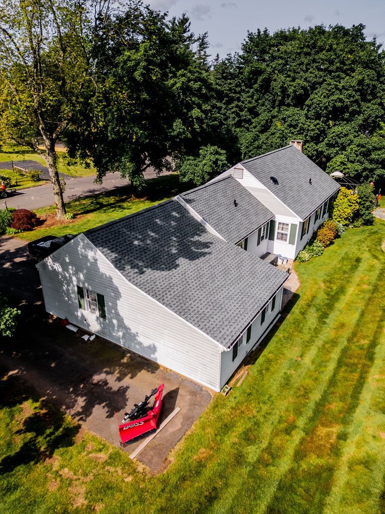 White house with gray roof, green lawn, and a red lawnmower, set on a sunny day.