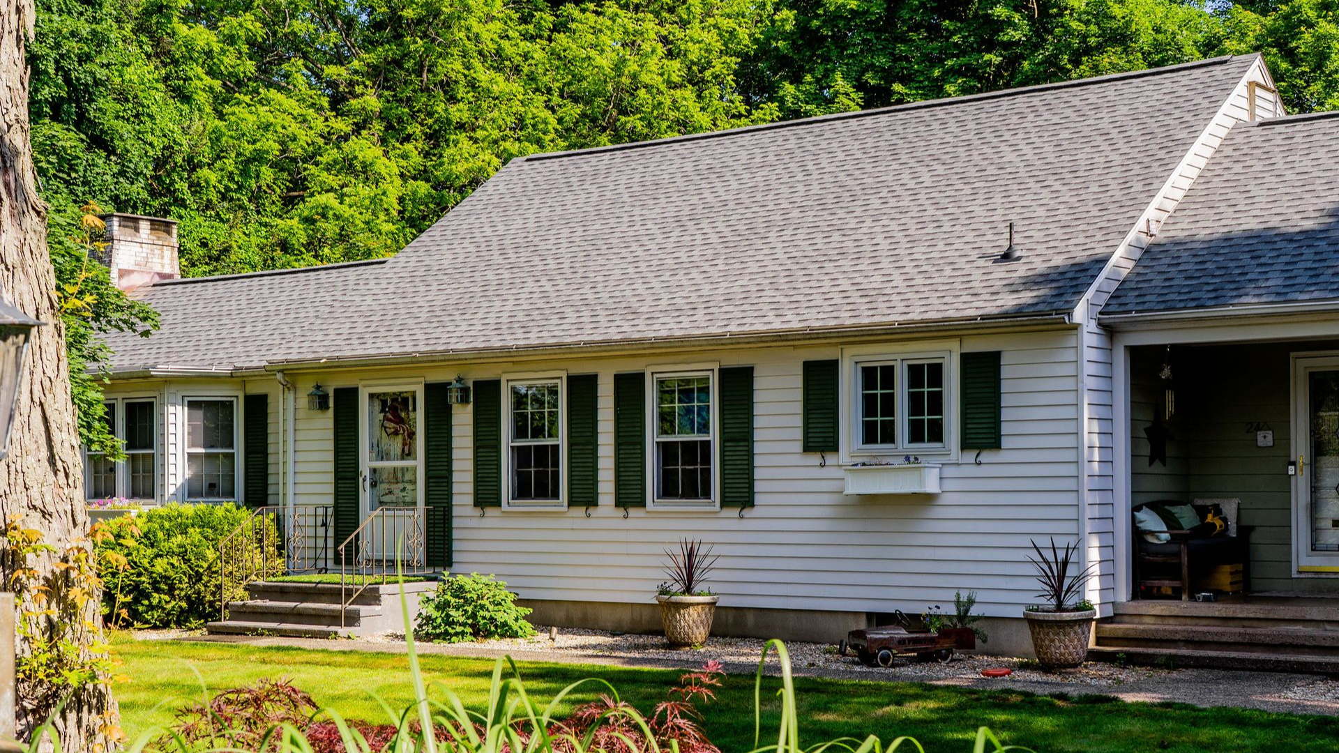 White house with gray roof, green shutters, and lush green trees.