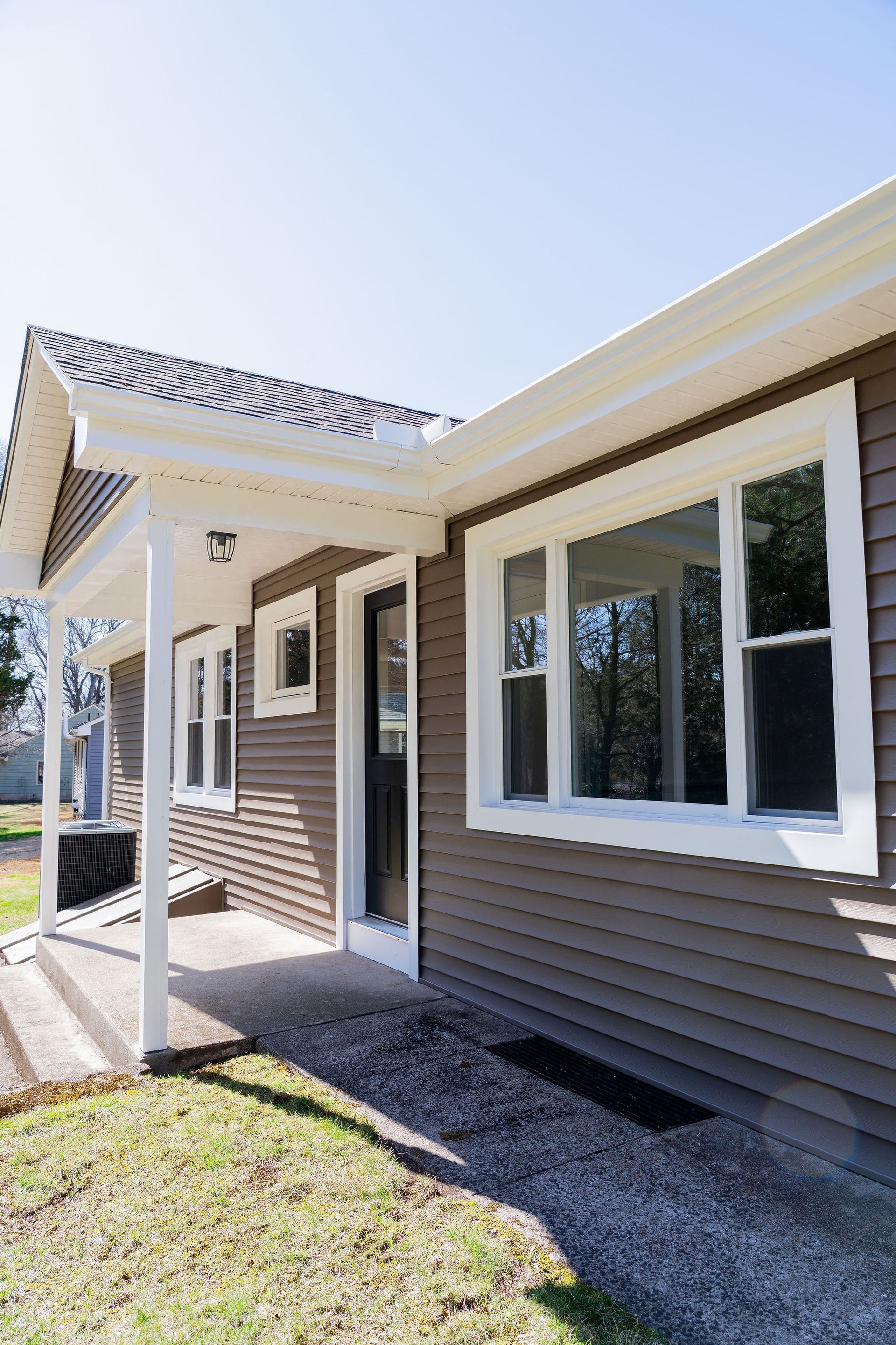 Brown house with white trim and windows, front porch, and green lawn.