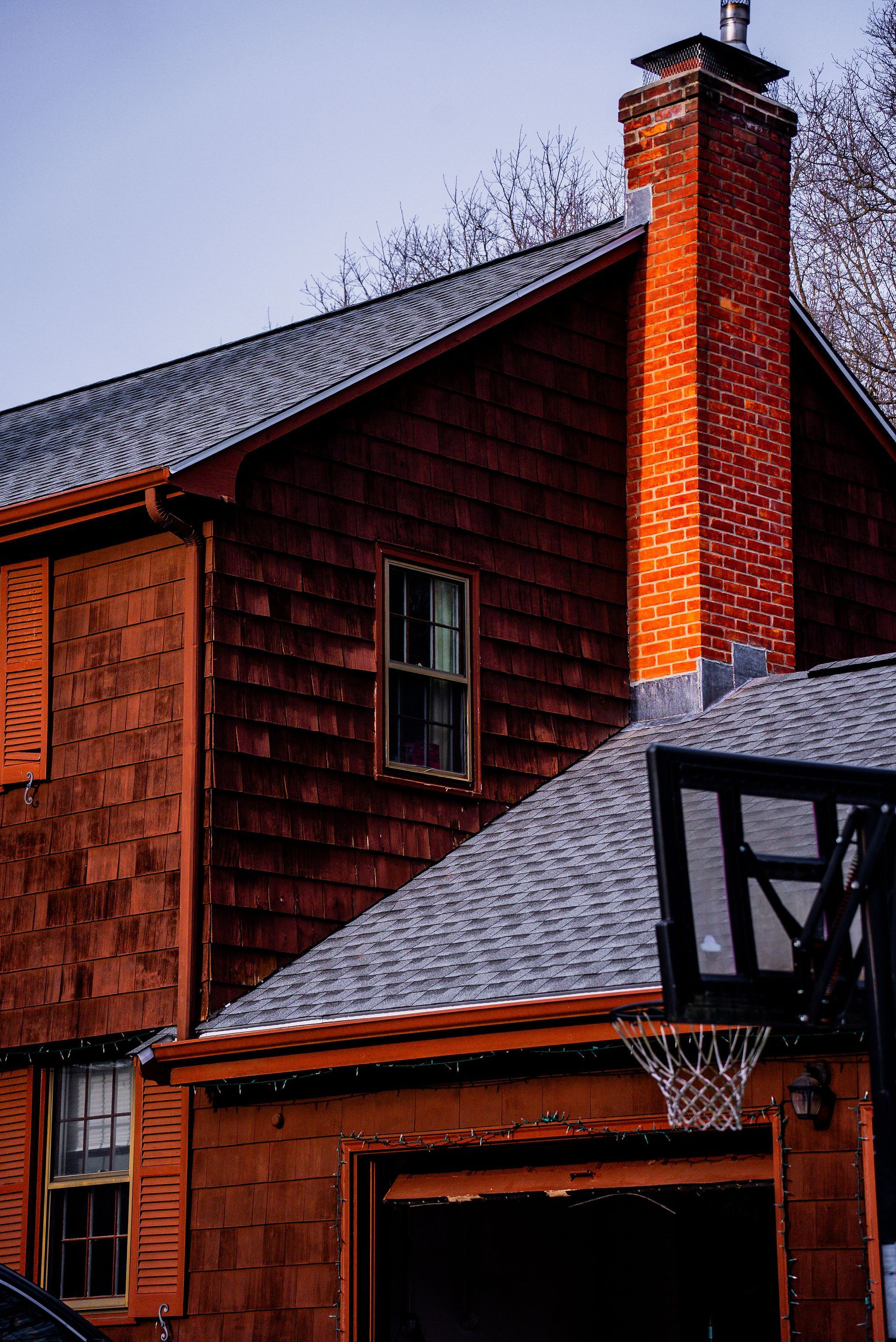 Two-story reddish house with a tall brick chimney next to a basketball hoop.