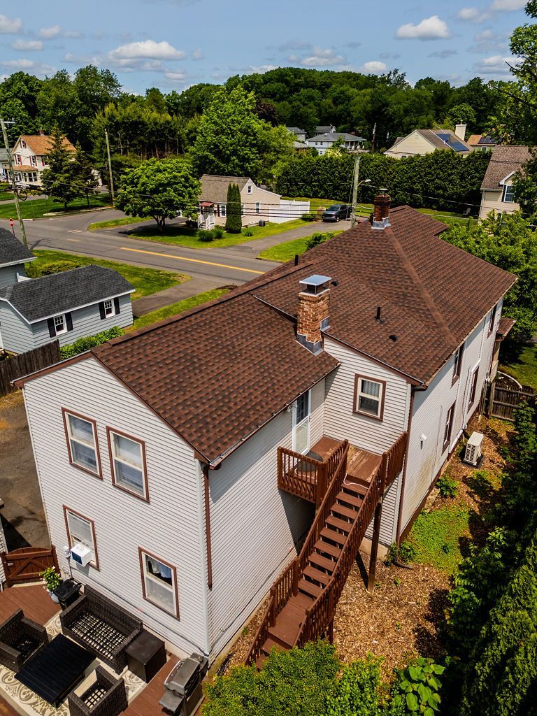 A two-story house with brown roof and wooden deck, nestled in a green, suburban neighborhood.