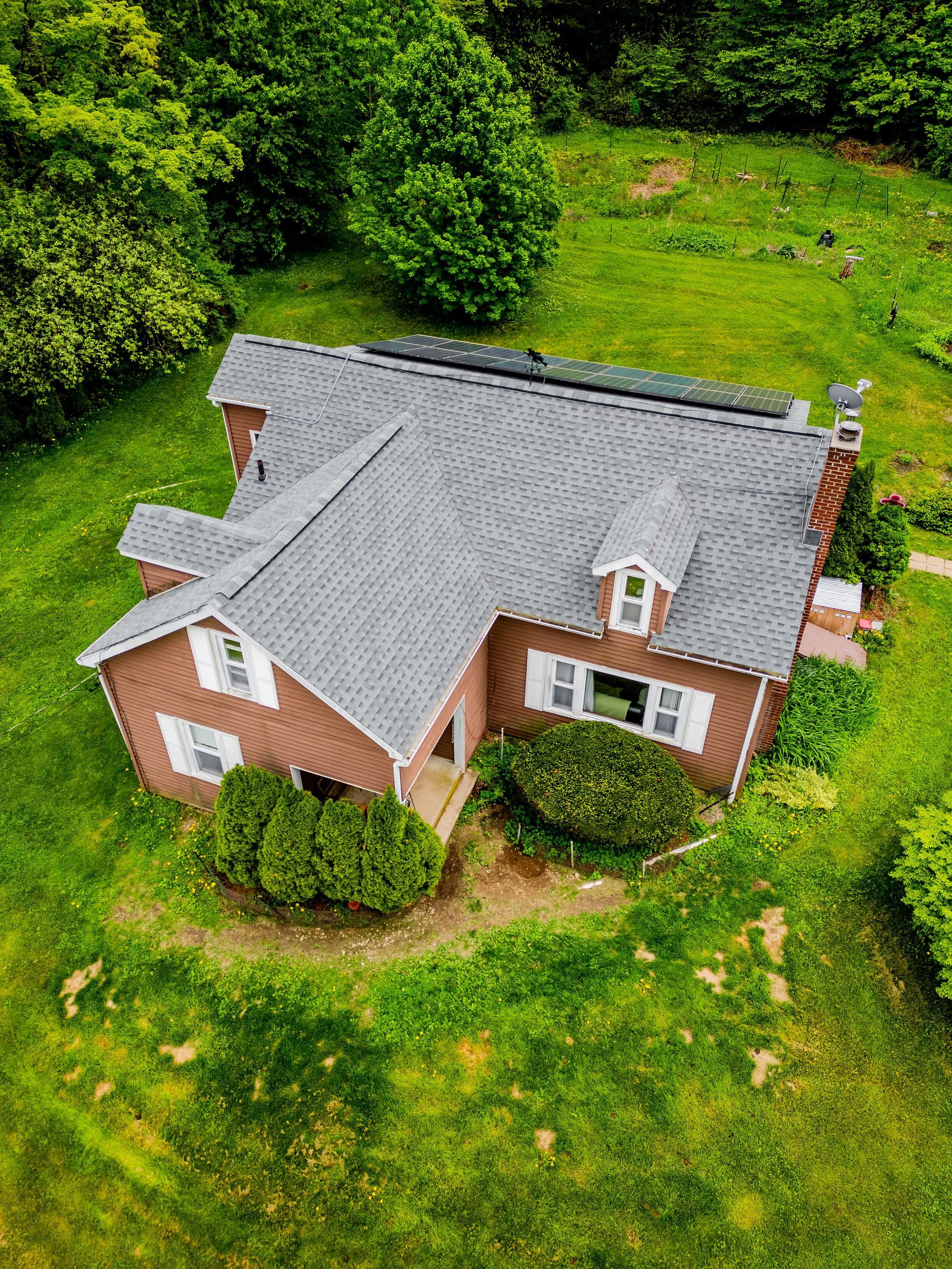 Brown house with gray roof on green grass. White window shutters.