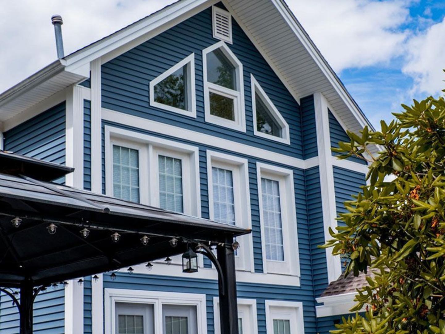 Blue house with white trim, gazebo in foreground, trees, and partly cloudy sky.