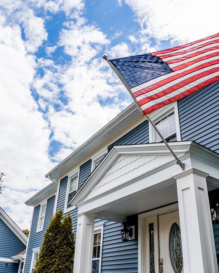 An american flag is hanging from the roof of a blue house.