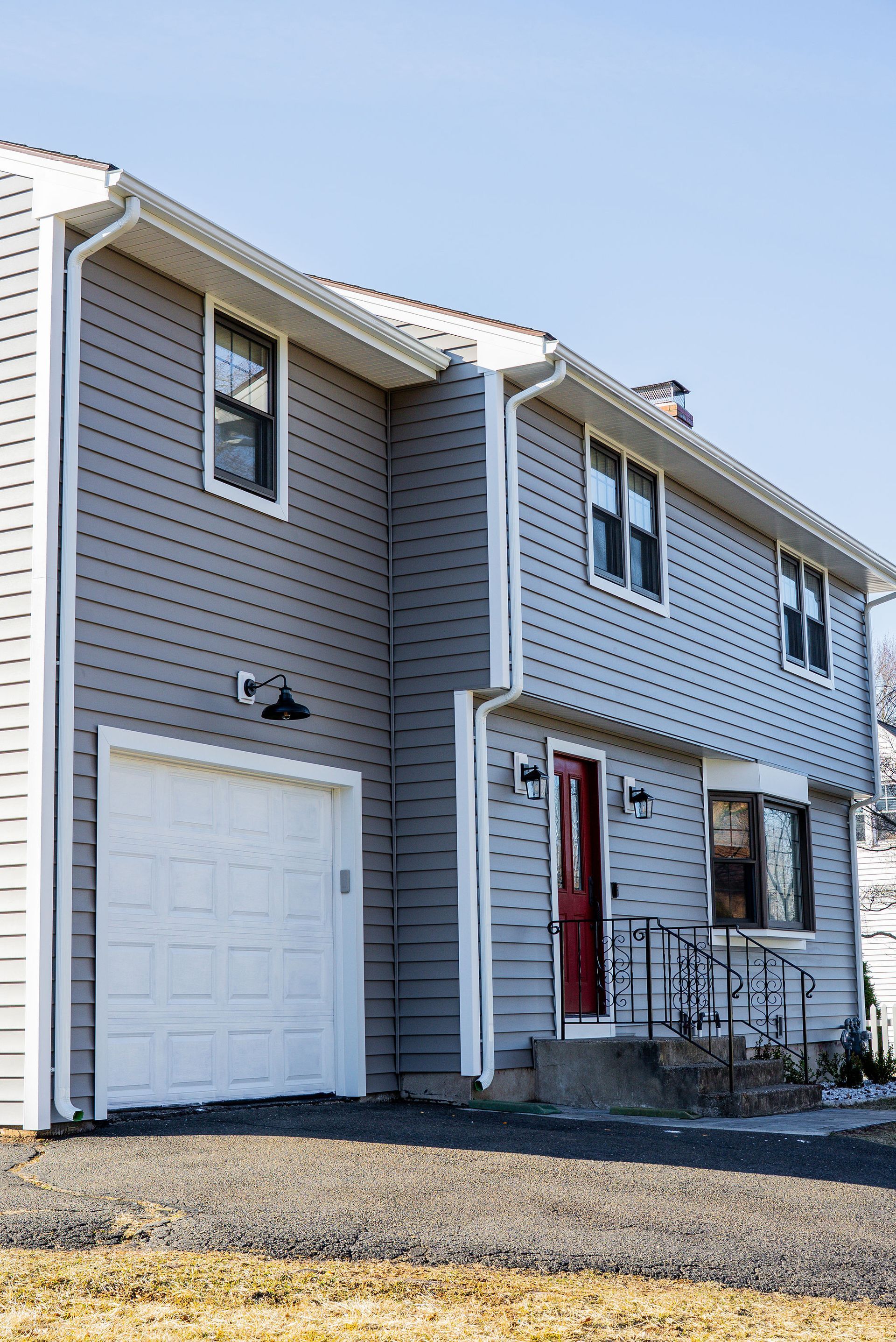 Two-story gray house with white garage door and red front door; sunny outdoor setting.