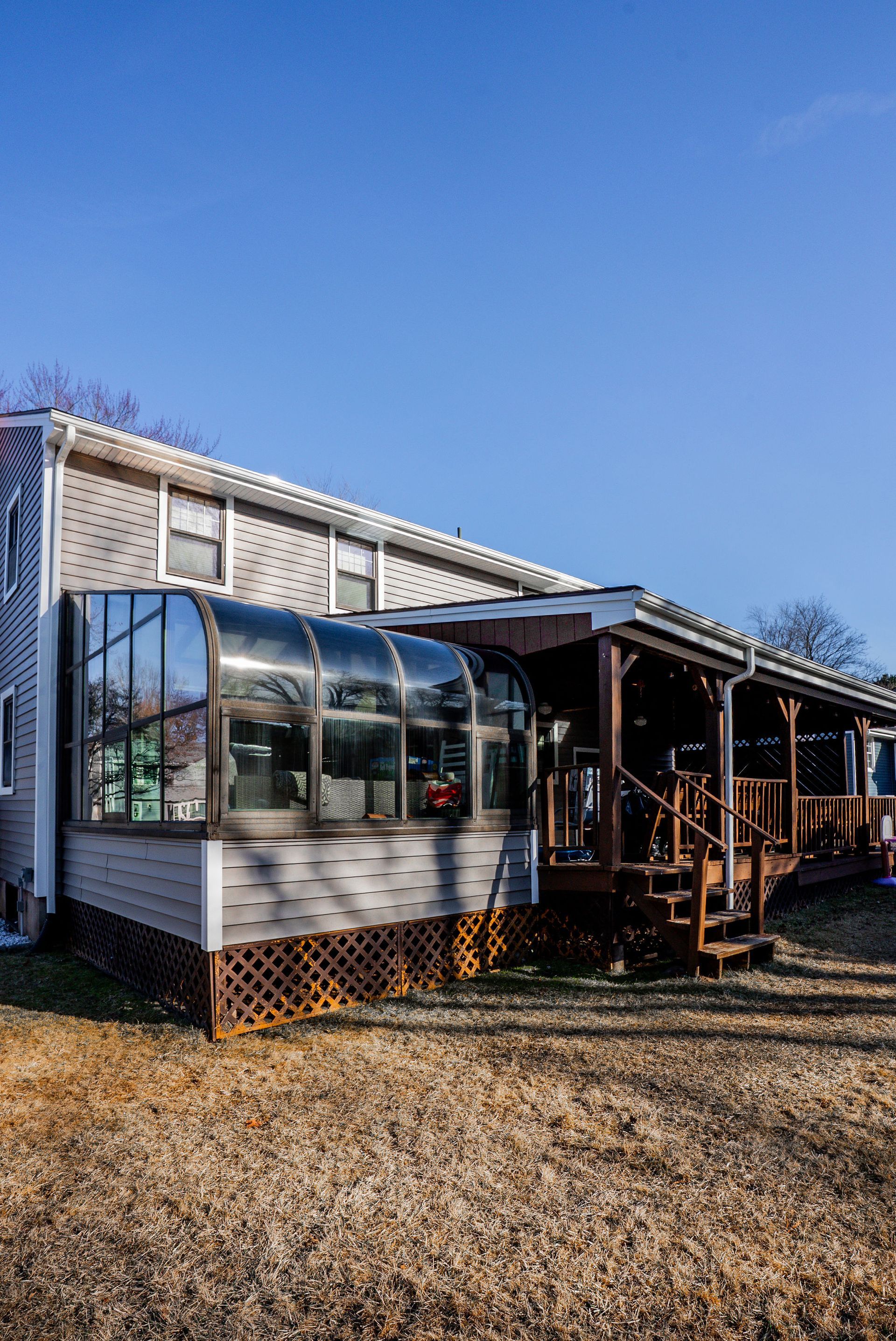 House with glass sunroom and wooden deck on a sunny day.