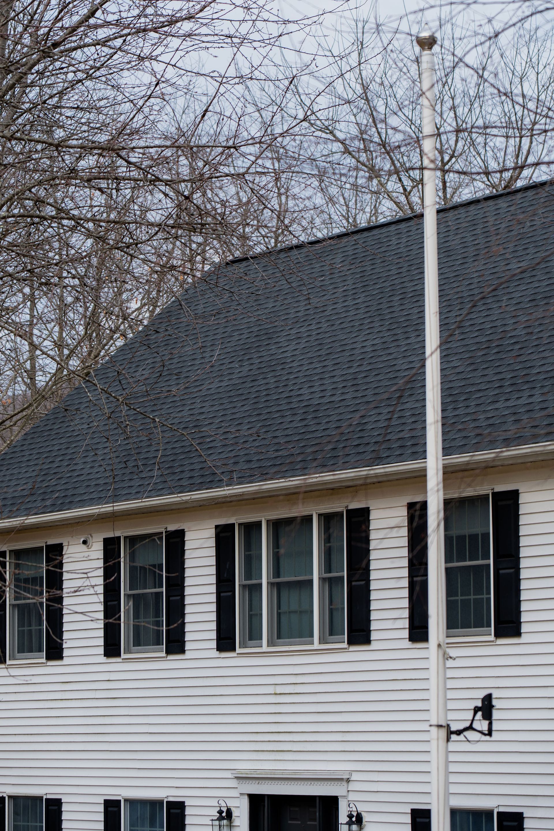 Two-story white house with black shutters and roof, flagpole stands tall.