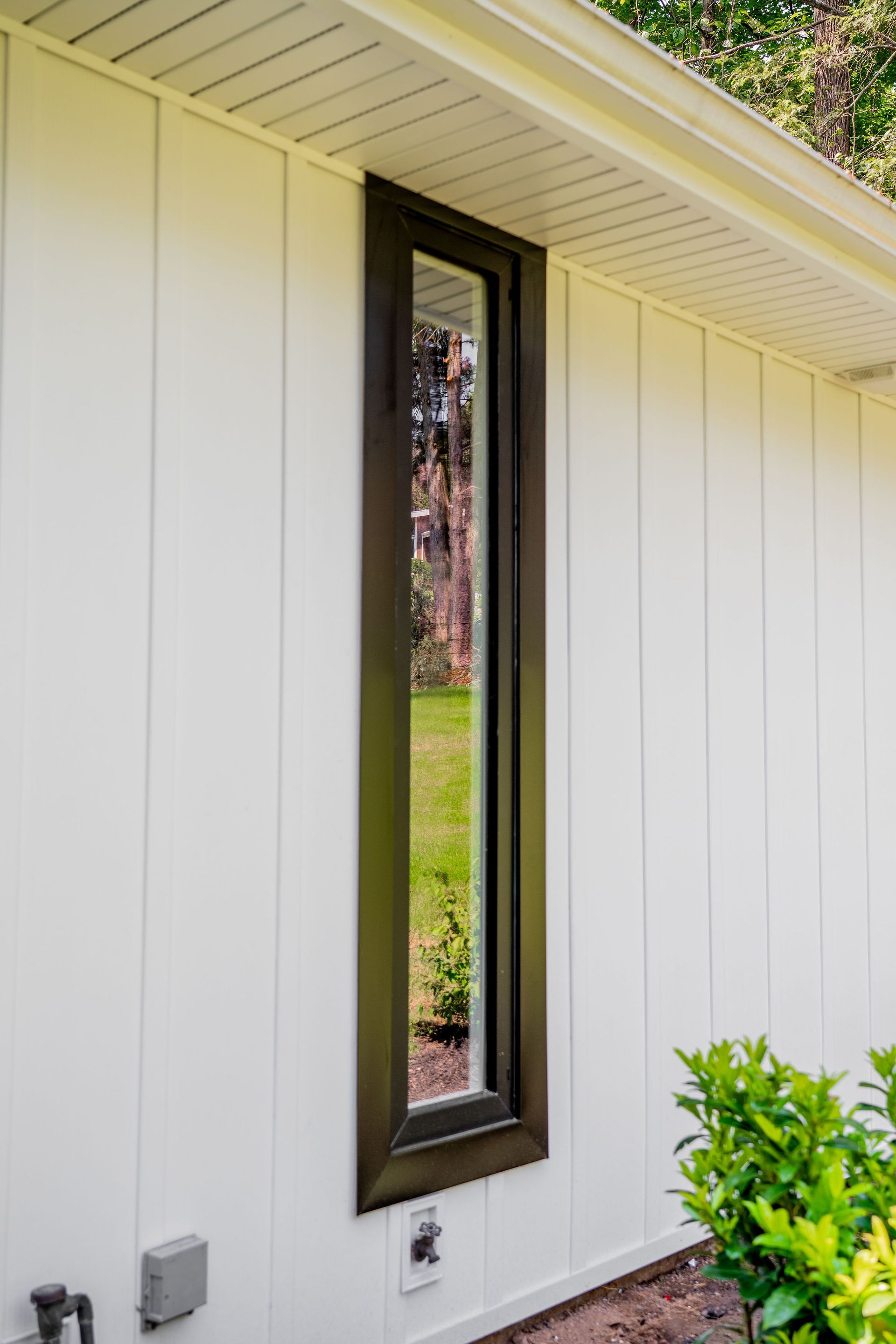Tall, dark-framed window on white siding. Green yard visible through the glass.