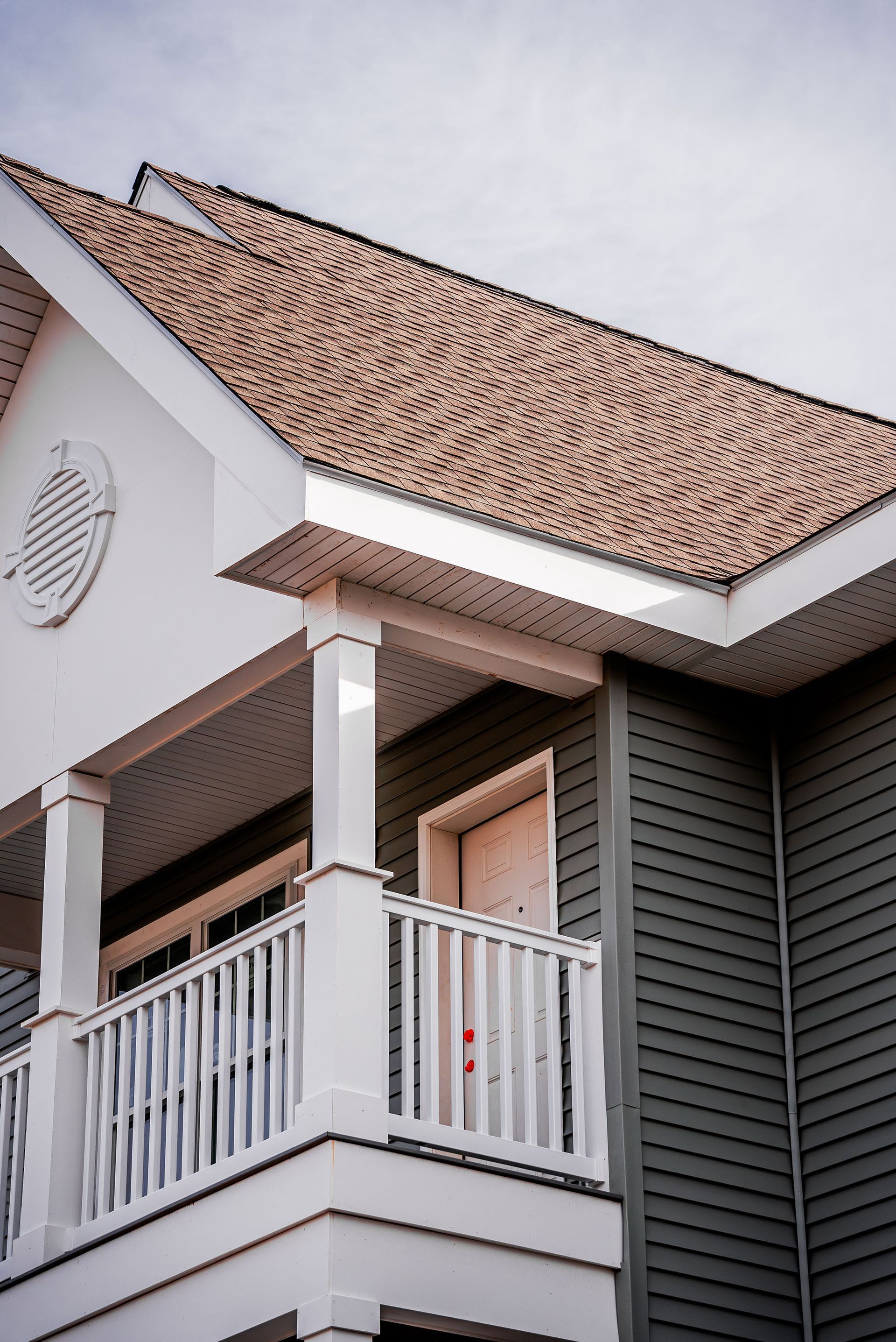 Two-story building with white porch and railing, green siding, and brown roof.