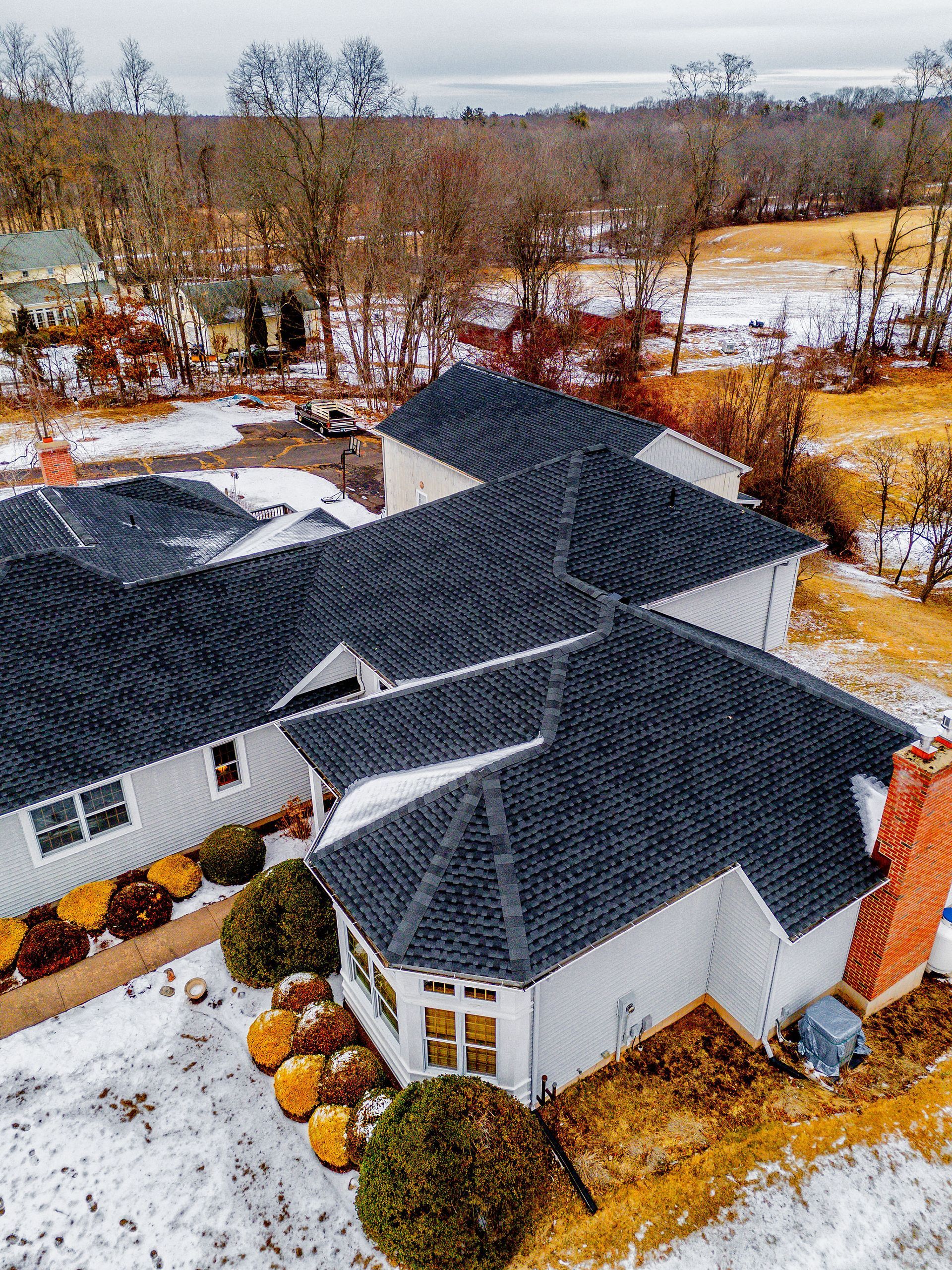 White house with dark roof, snow-covered ground, and leafless trees in a rural winter setting.