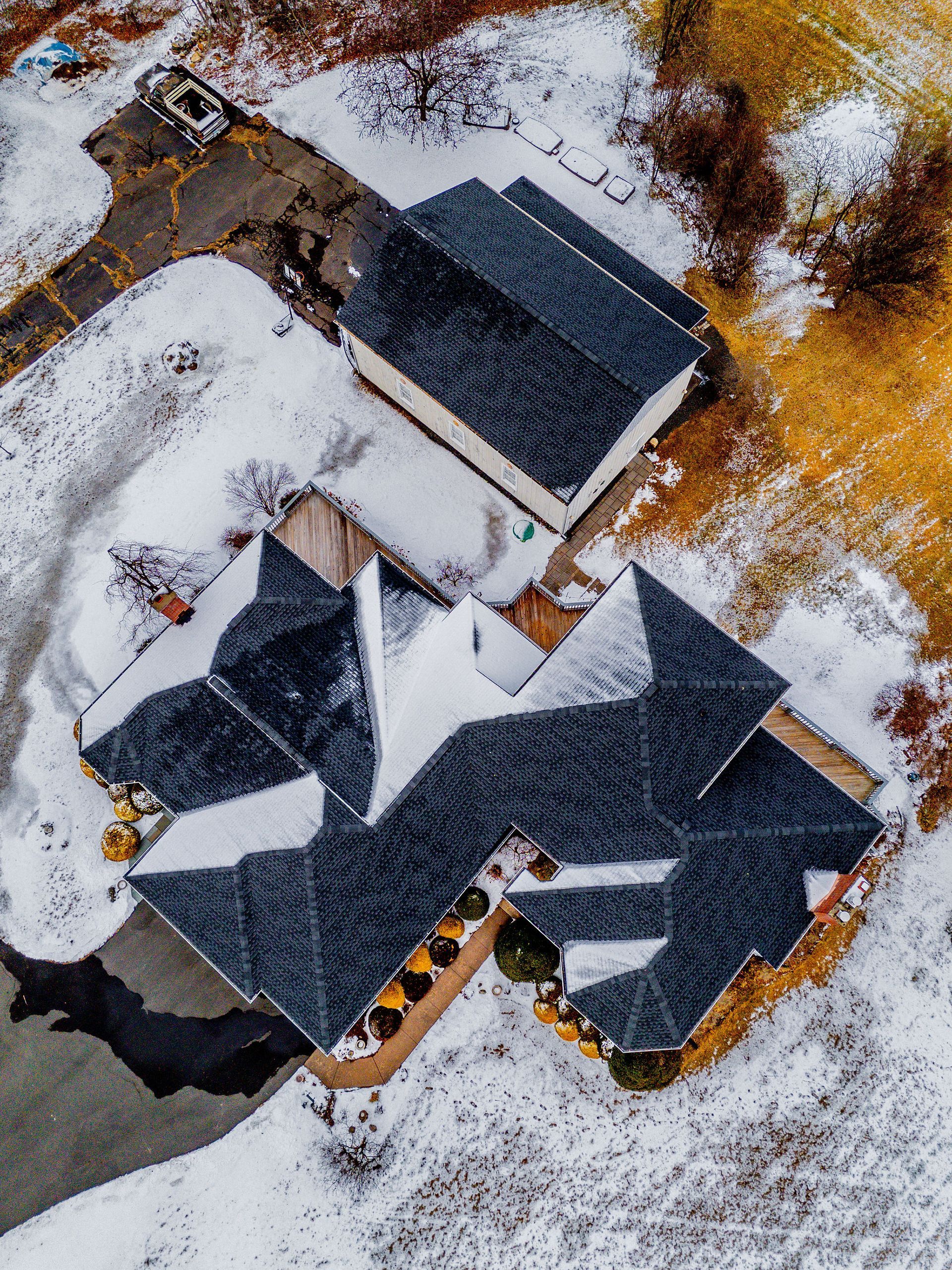 Aerial view of a house and detached garage covered in snow. Grey roofs, white snow, and brown yard.
