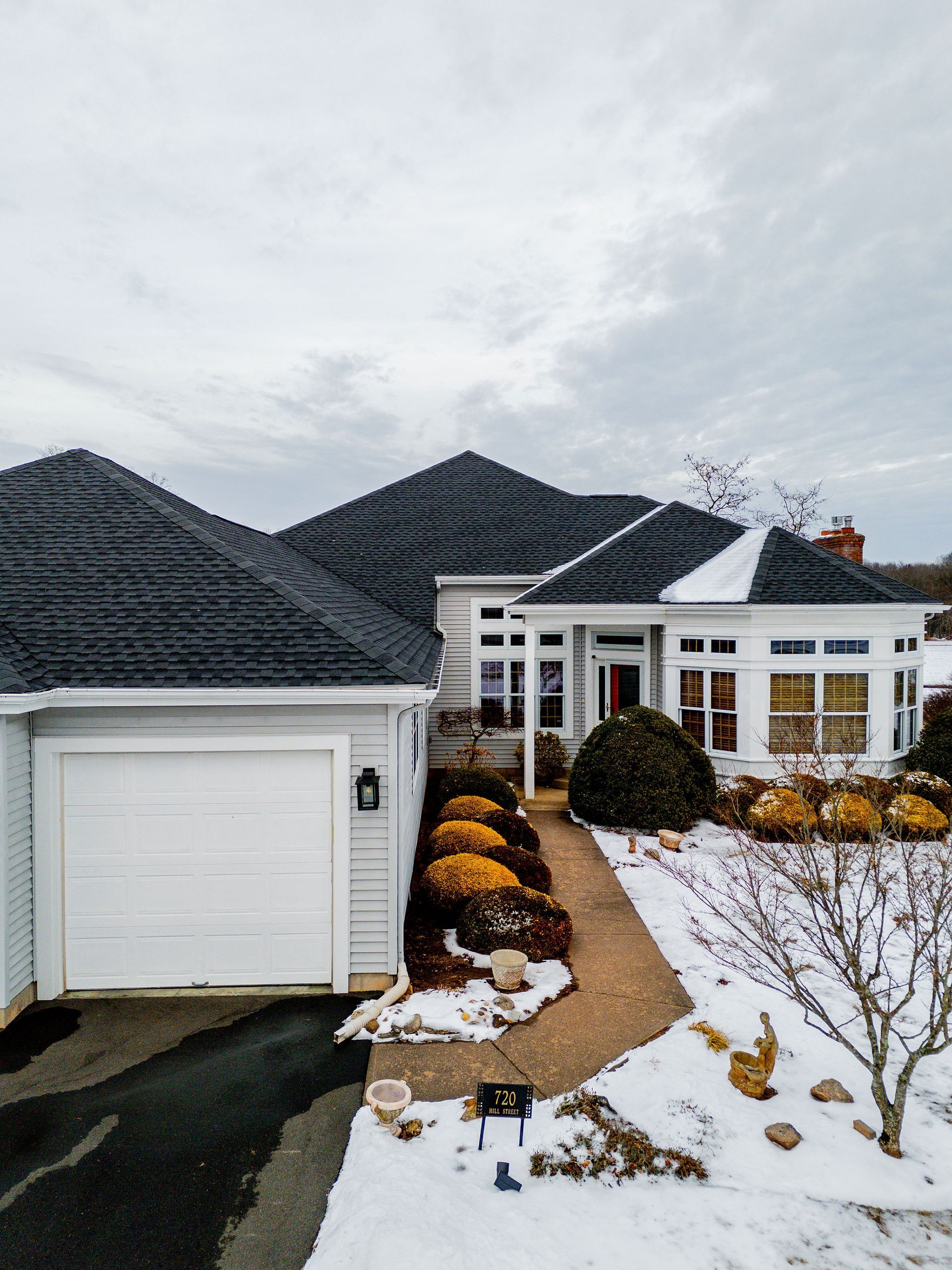 House with dark roof, white siding, garage, and snowy walkway.