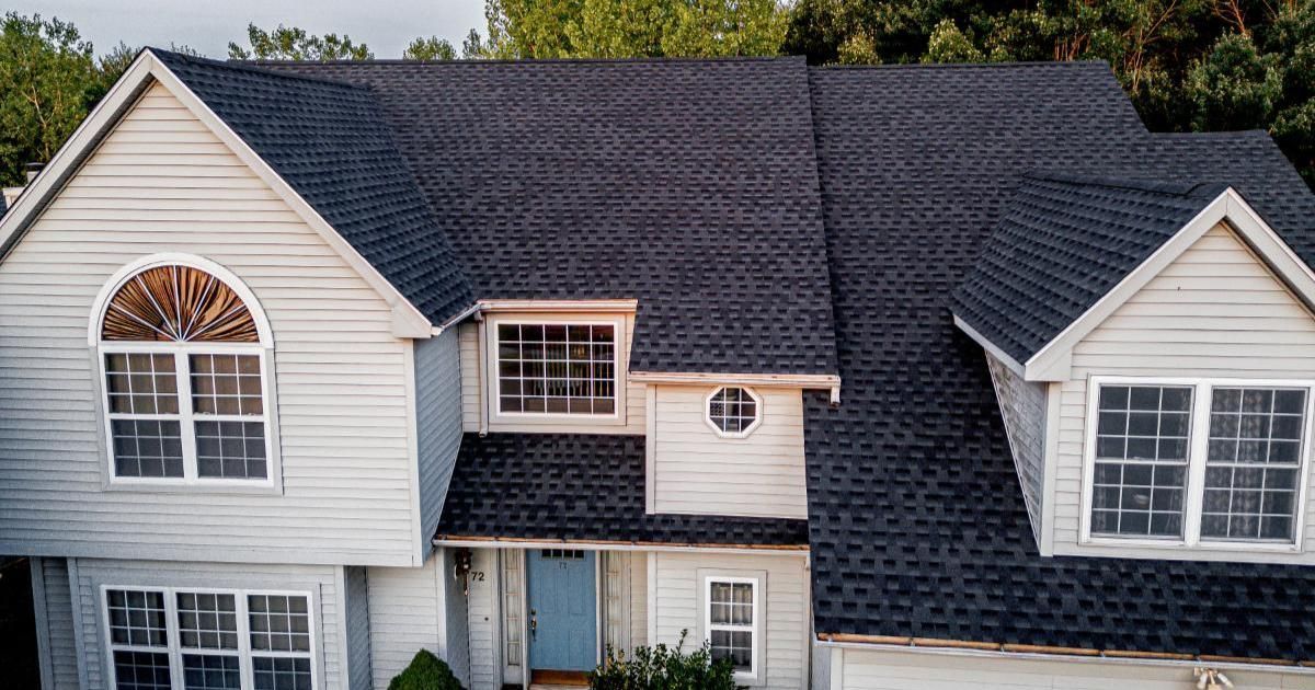 An aerial view of a large white house with a black roof.