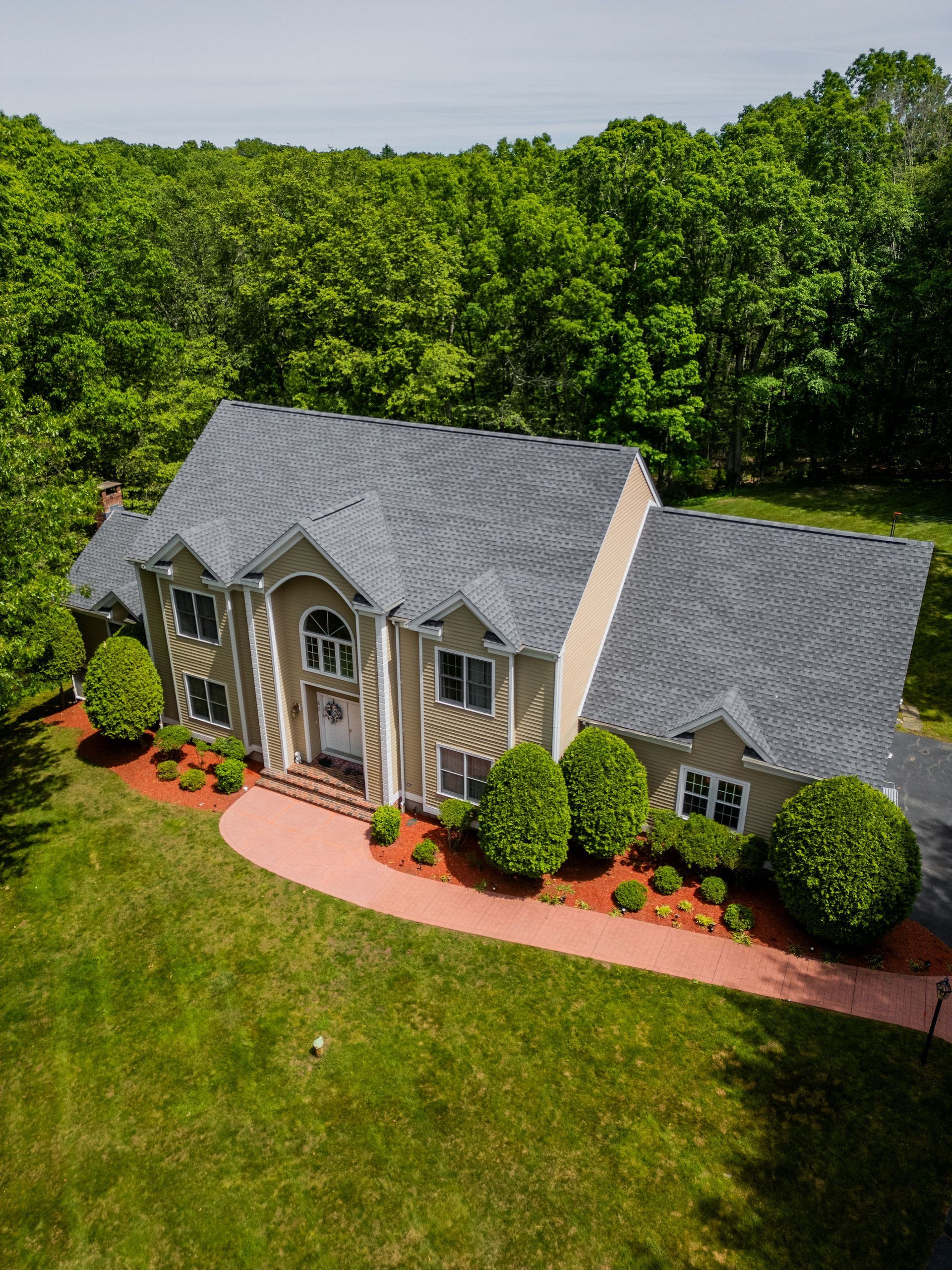 Large beige house with gray roof, trees in background, red pathway leading to the front door, green grass.
