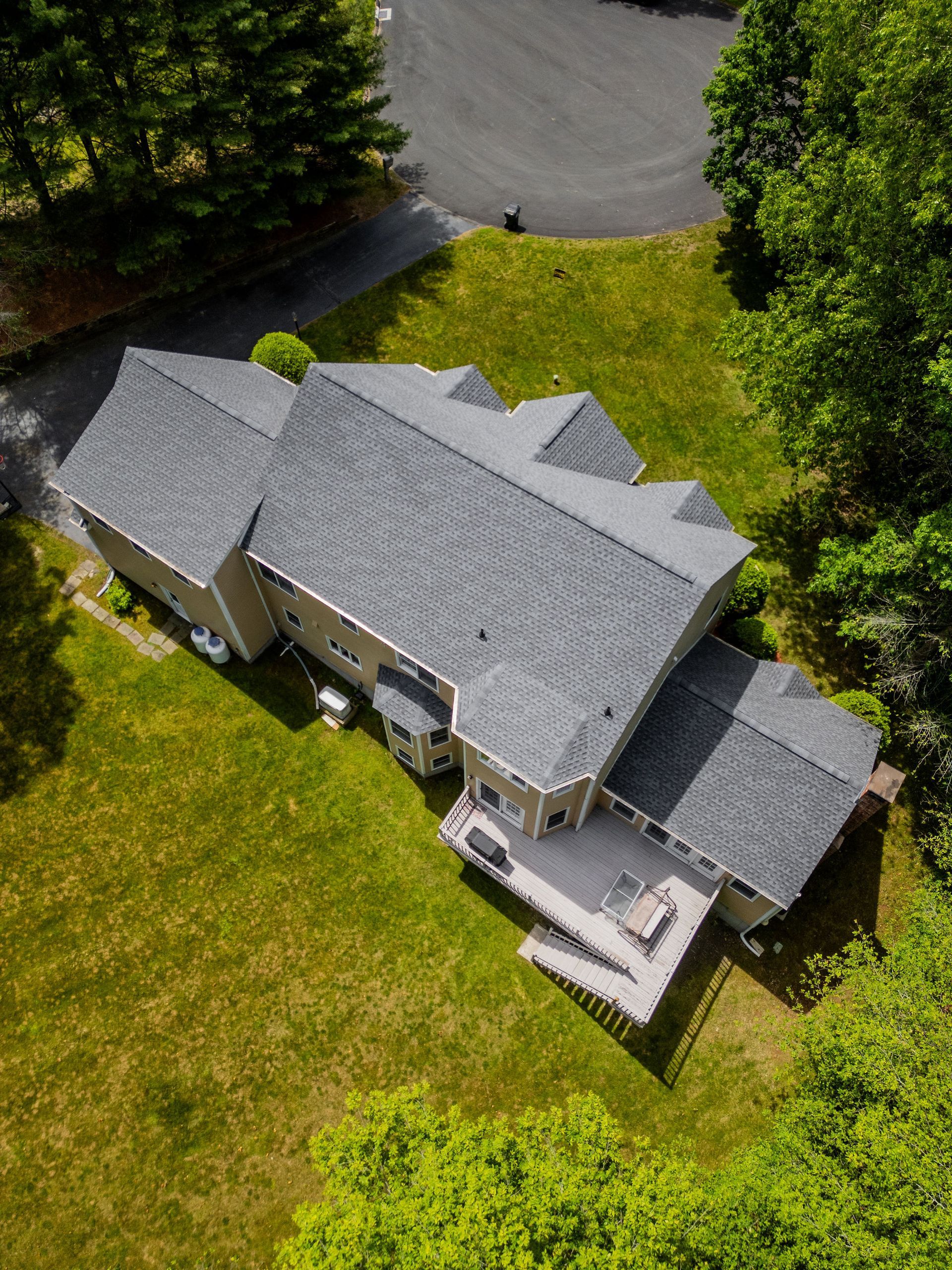 Aerial view of a house with a gray roof, surrounded by green grass and trees.