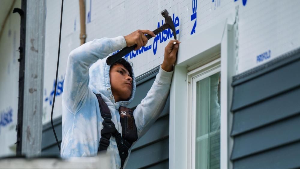 A man is hammering a nail into the side of a house.