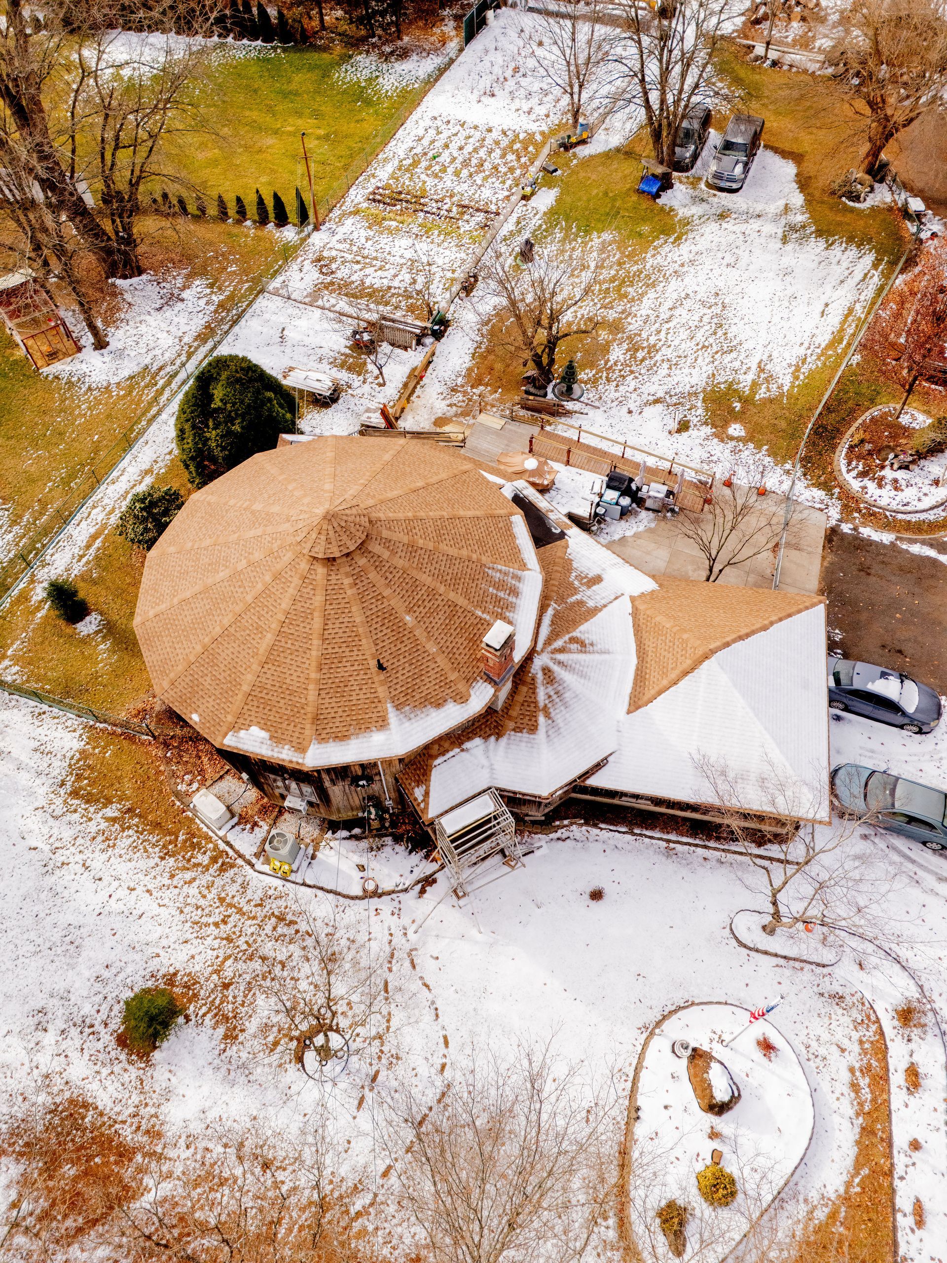 Overhead view of a house with a large, round roof covered in snow, surrounded by a snowy yard.