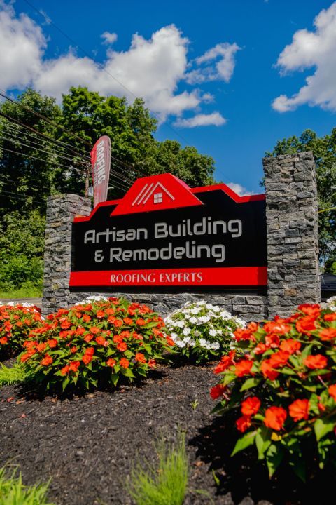 A sign for artisan building and remodeling surrounded by flowers