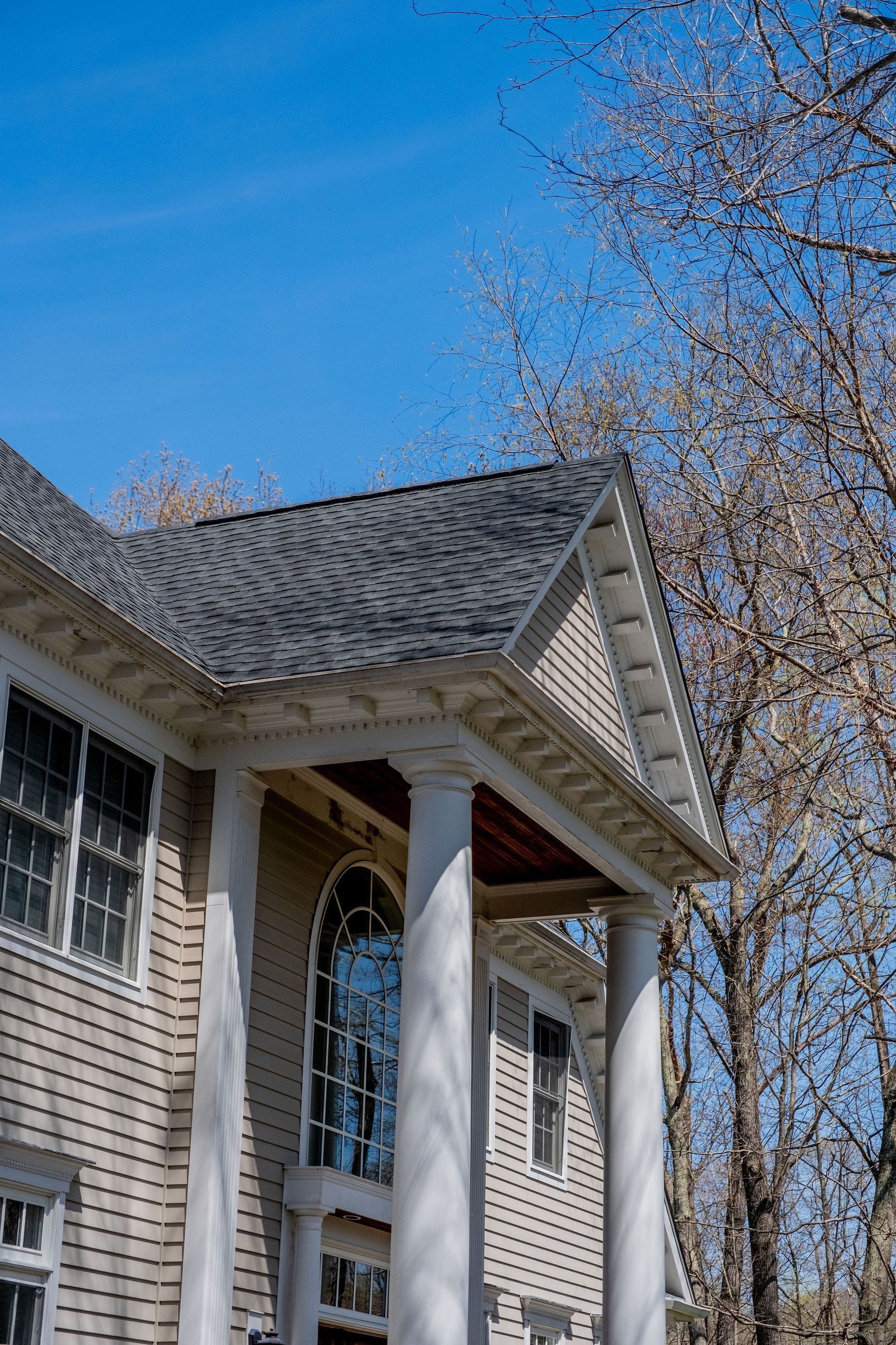 Beige house with white columns, gray roof, and a clear blue sky.