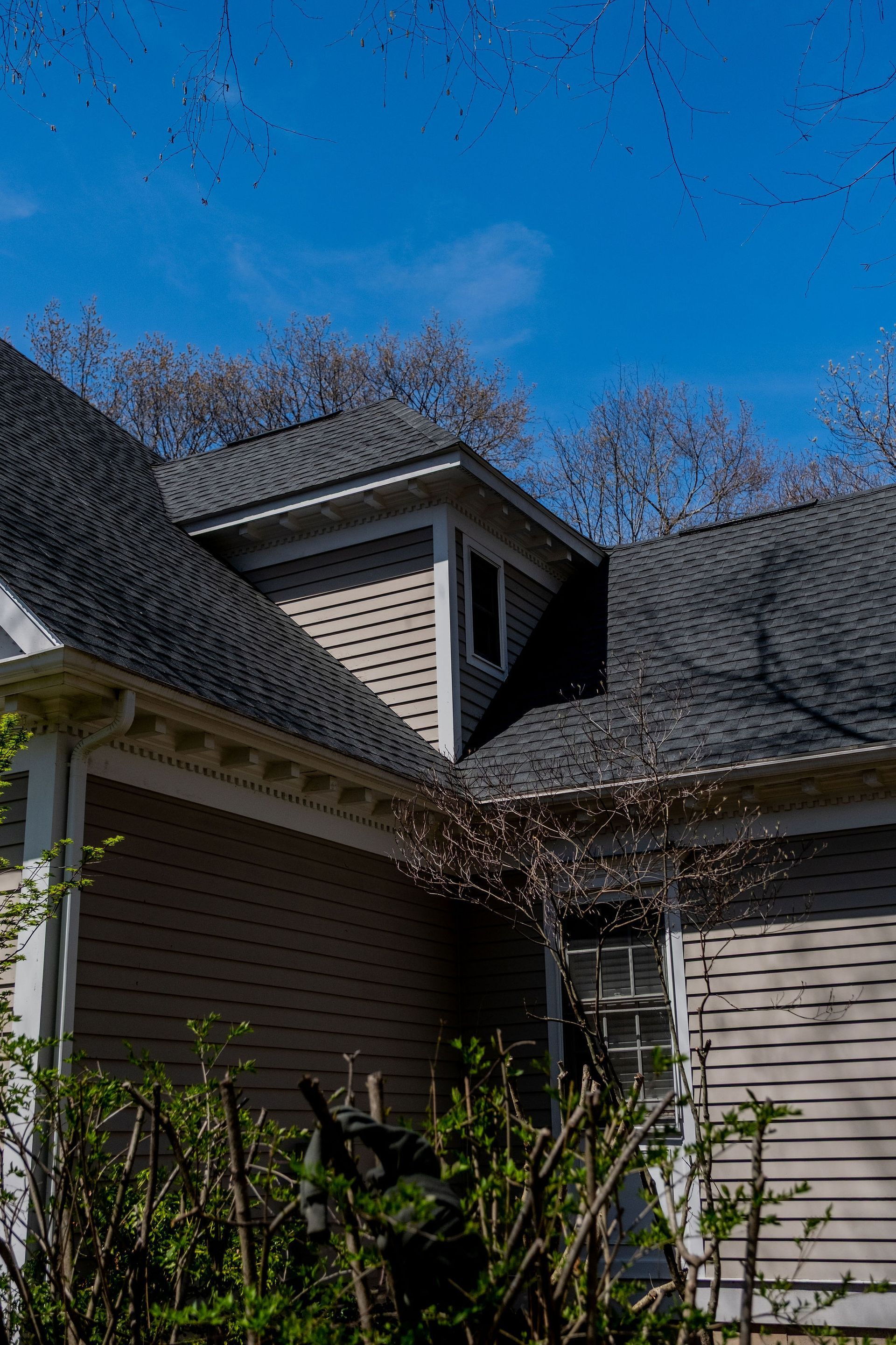 House exterior with a dormer, brown siding, and a blue sky.