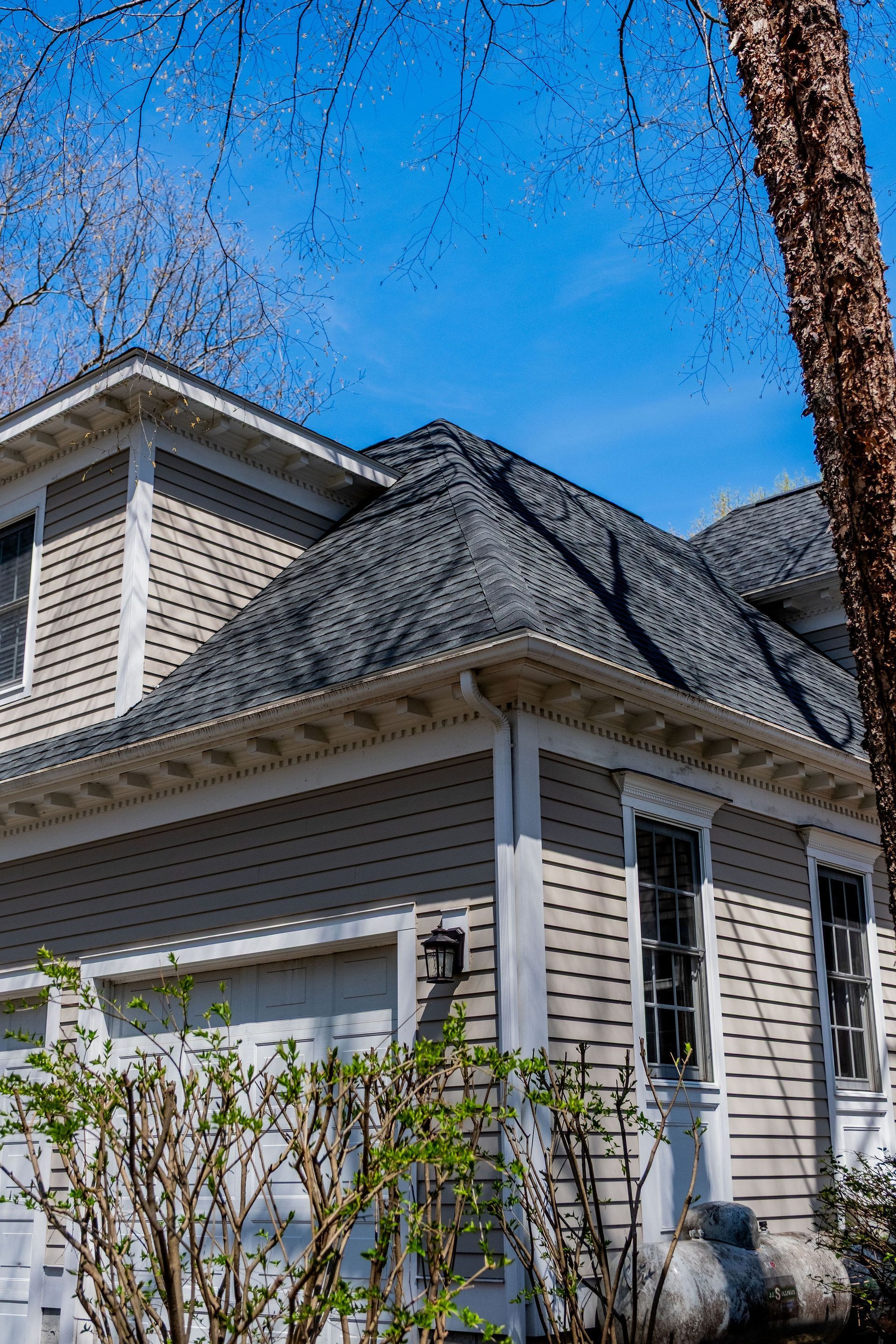 Tan house with gray roof, white trim, and blue sky background.