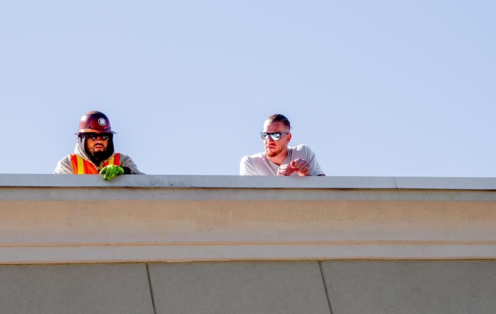 Two construction workers are standing on the edge of a building.