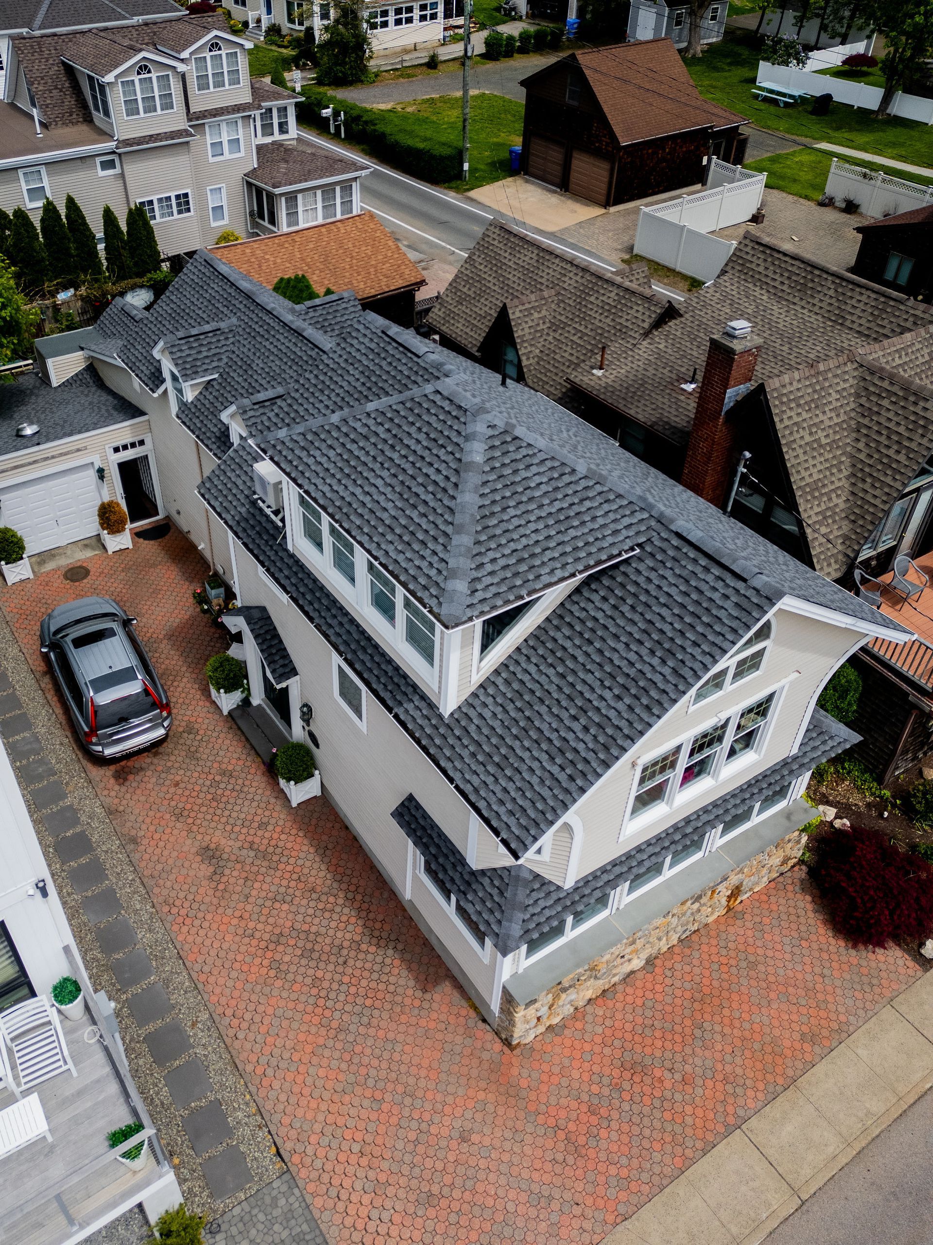 Overhead view of a two-story house with a brick driveway and grey roof. A car is parked in front.
