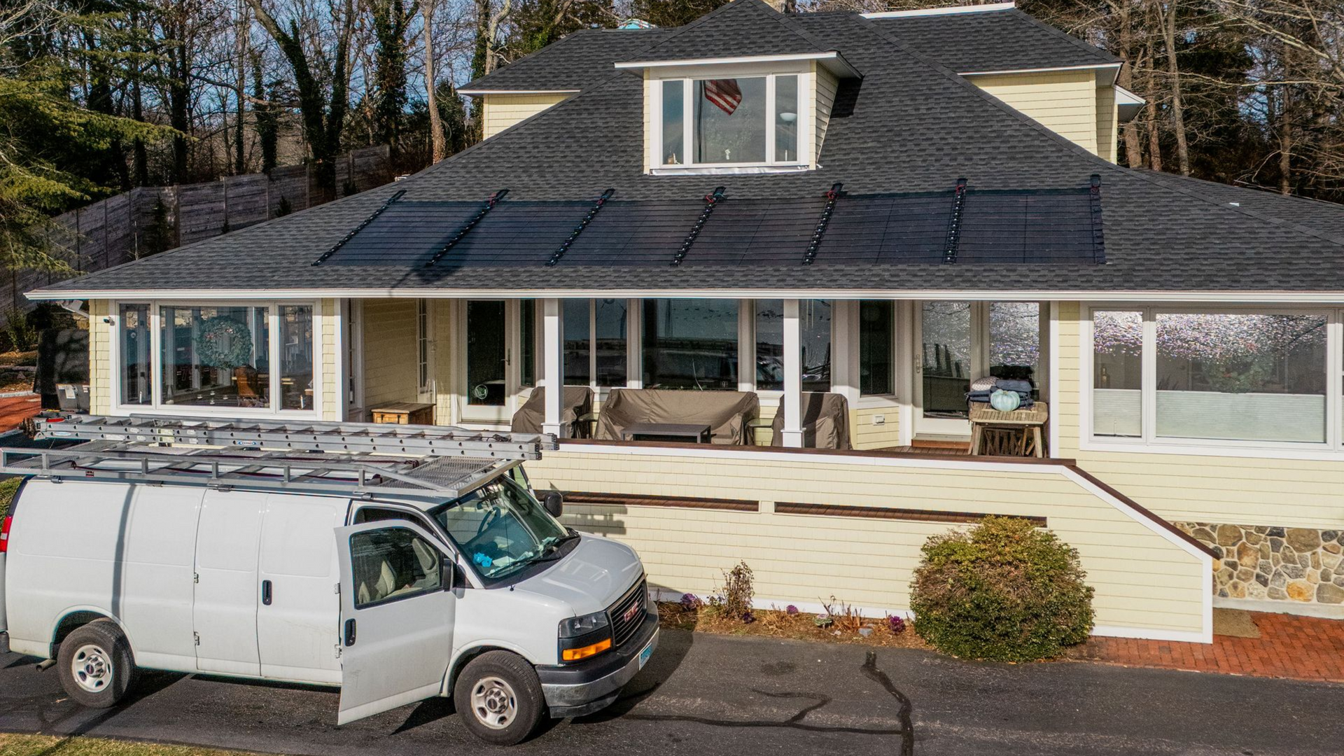 White van parked in front of a yellow house with solar panels on the roof.