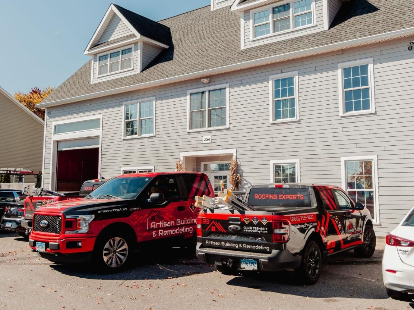 Two red company trucks parked in front of a gray building. One truck has the company logo.